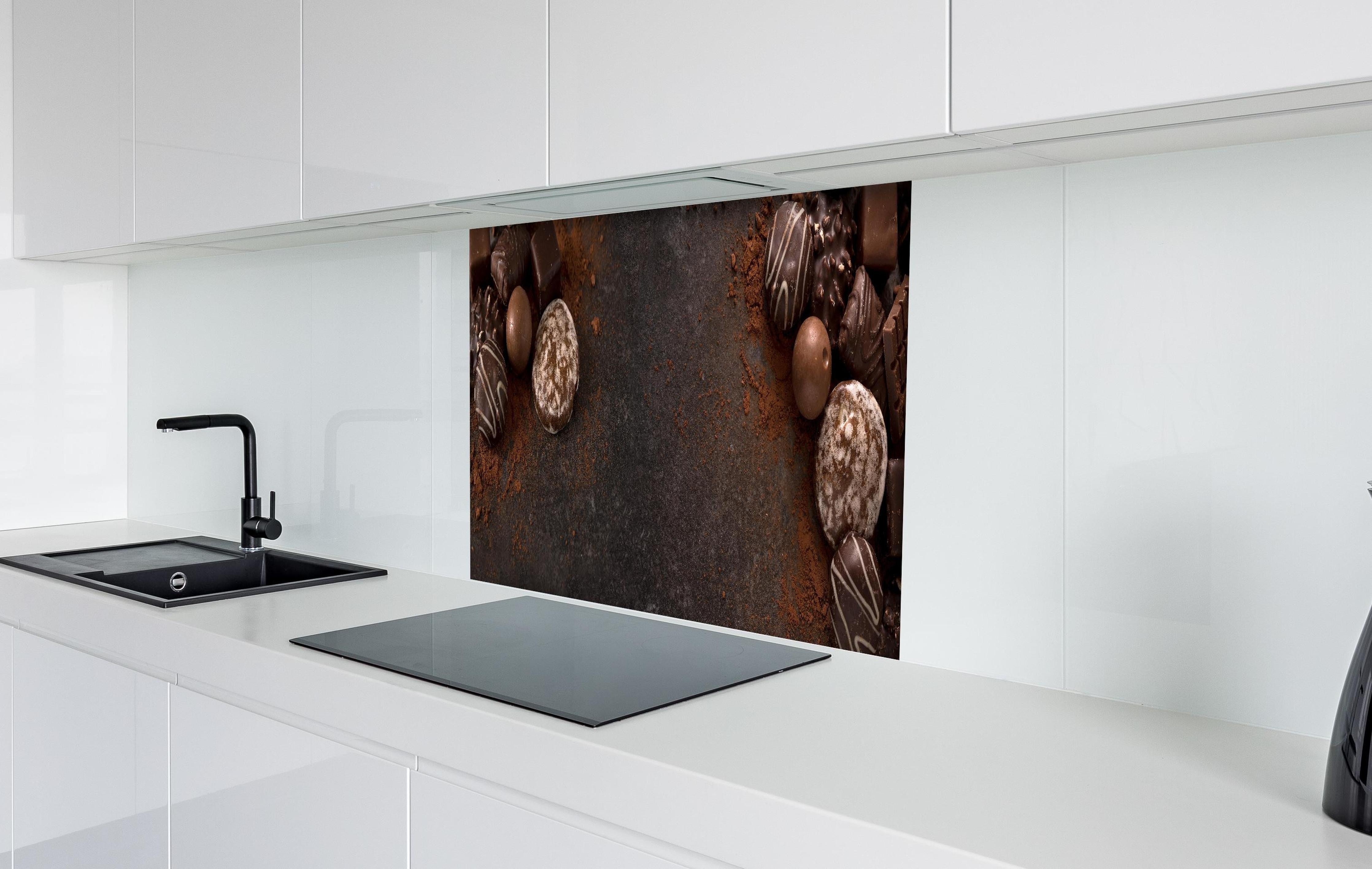 Spritzschutz - Schokoladenpralinen auf Schieferuntergrund hinter einem Cerankochfeld zwischen Holz-Kochutensilien
