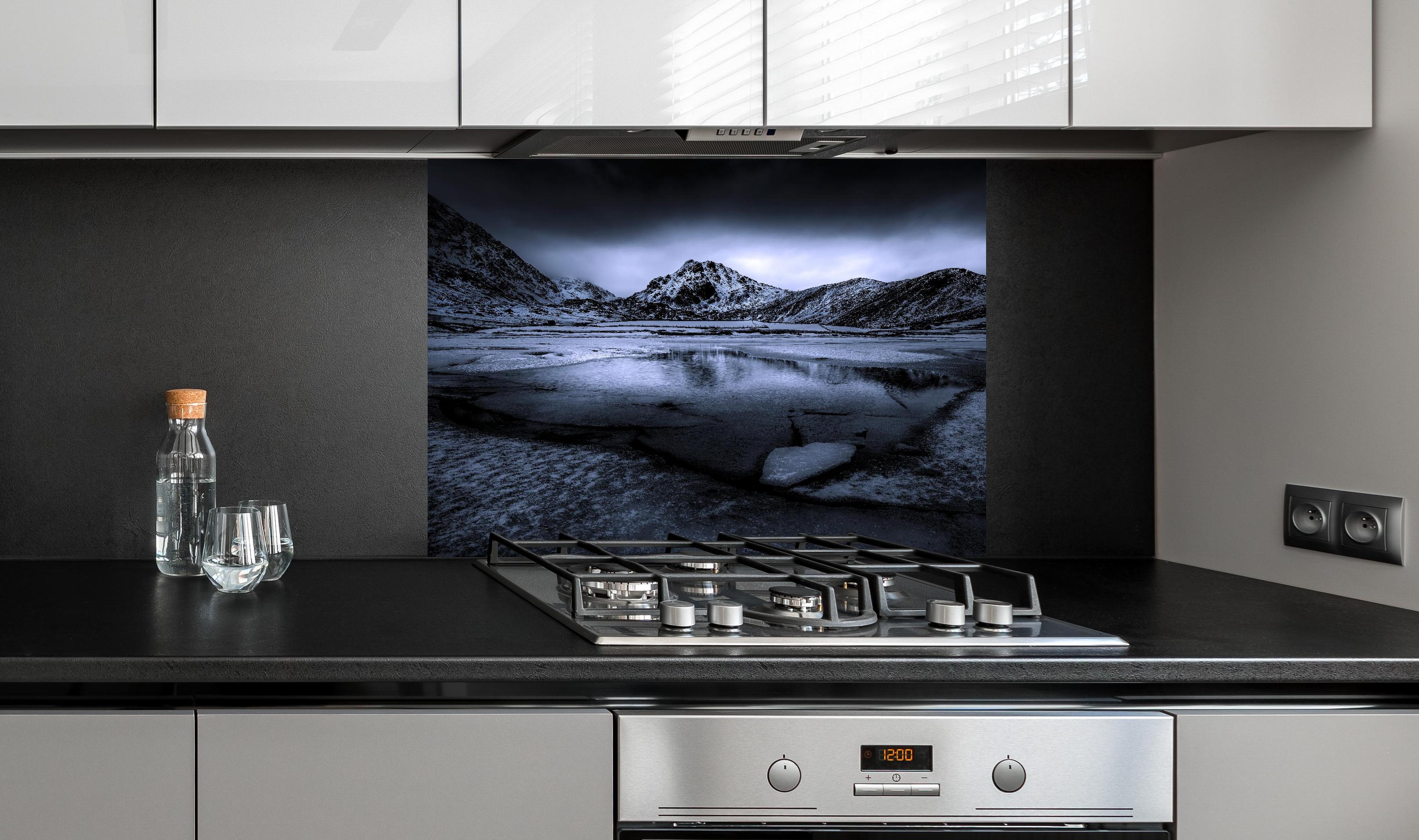 Spritzschutz - Schwarz-Weiß Winterlandschaft mit Bergspiegelung hinter einem Cerankochfeld zwischen Holz-Kochutensilien
