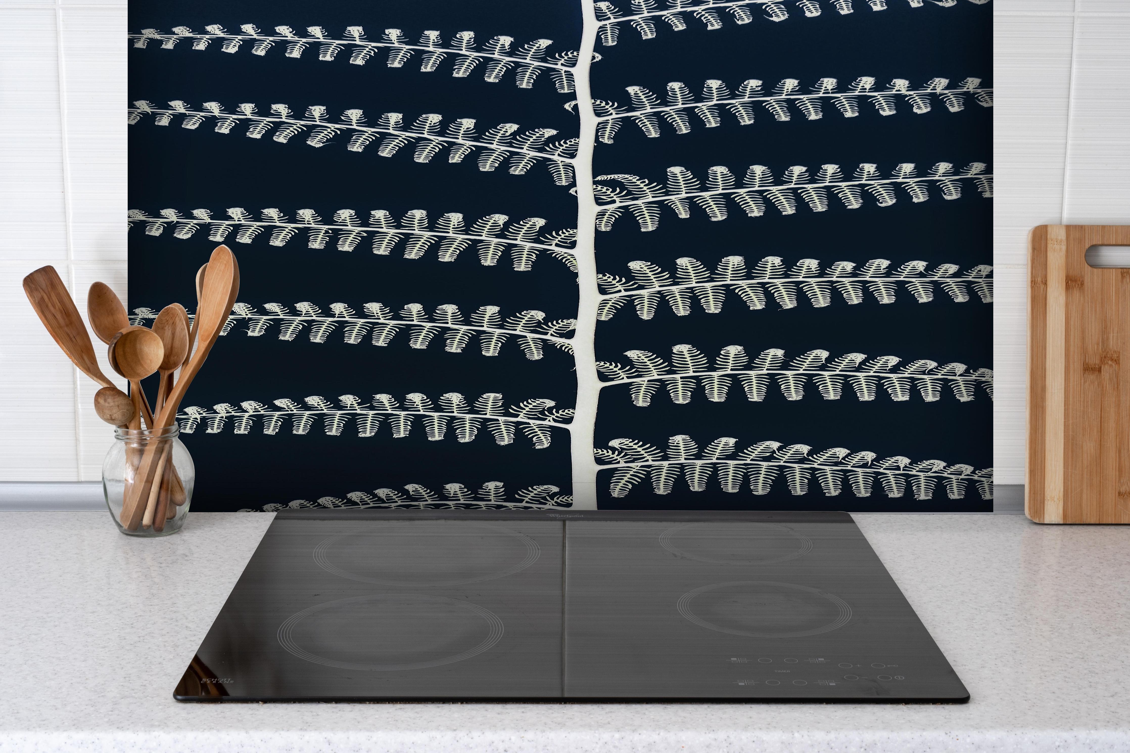 Spritzschutz - Schwarz-weißes Farnmuster auf dunklem Hintergrund hinter einem Cerankochfeld zwischen Holz-Kochutensilien
