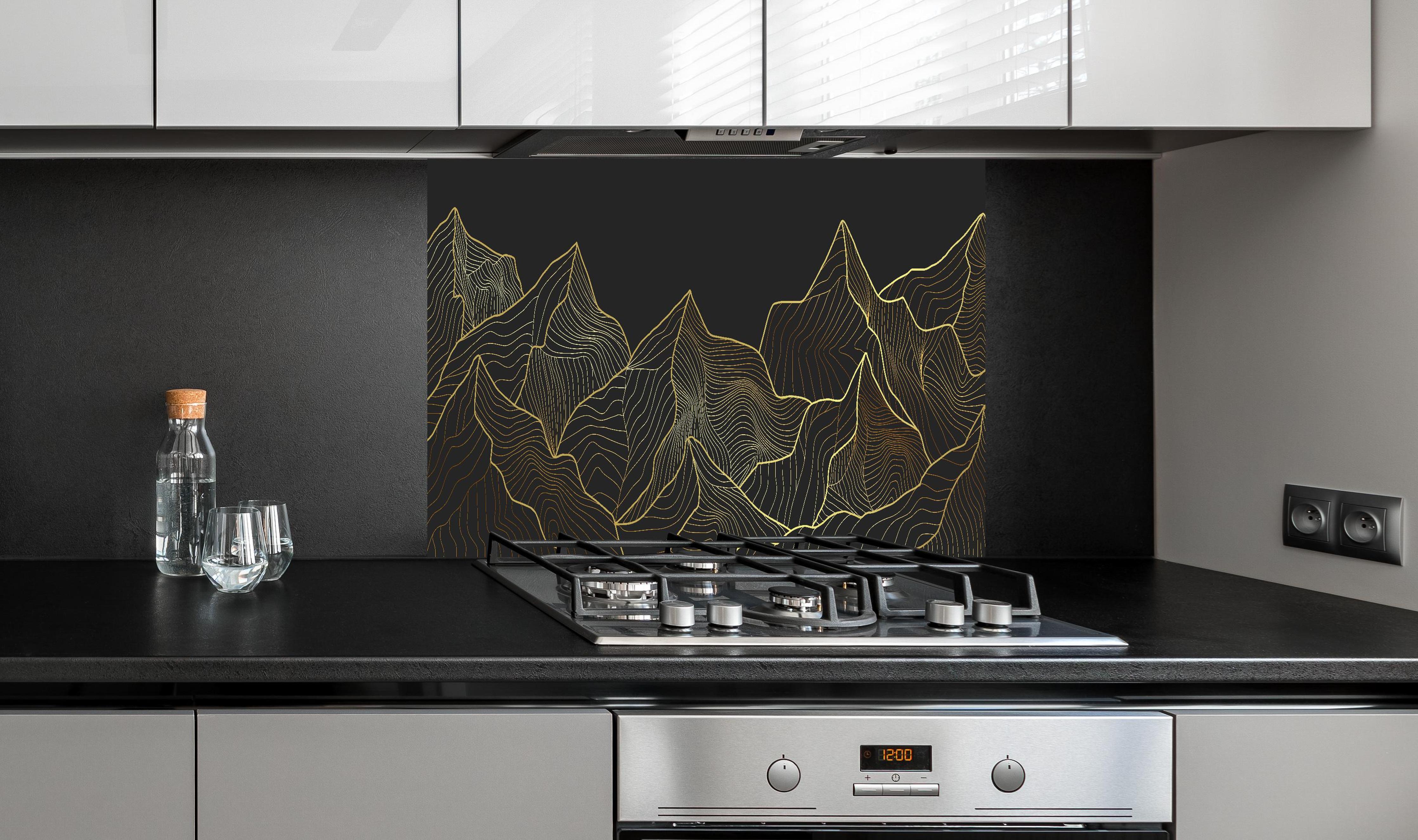 Spritzschutz - Schwarze Berge mit goldener Linienkunst hinter einem Cerankochfeld zwischen Holz-Kochutensilien
