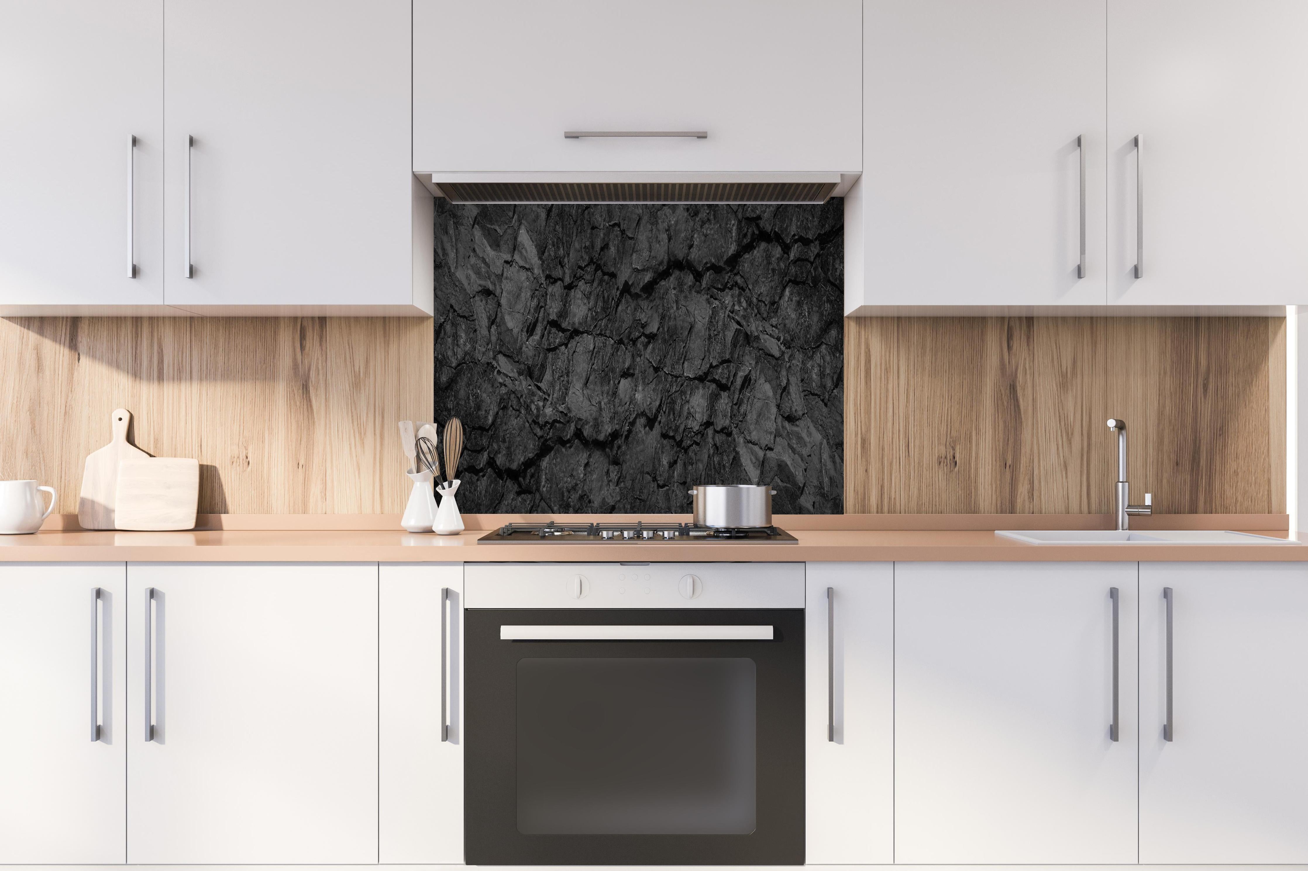 Spritzschutz - Schwarze Gesteinstextur mit Rissen hinter einem Cerankochfeld zwischen Holz-Kochutensilien
