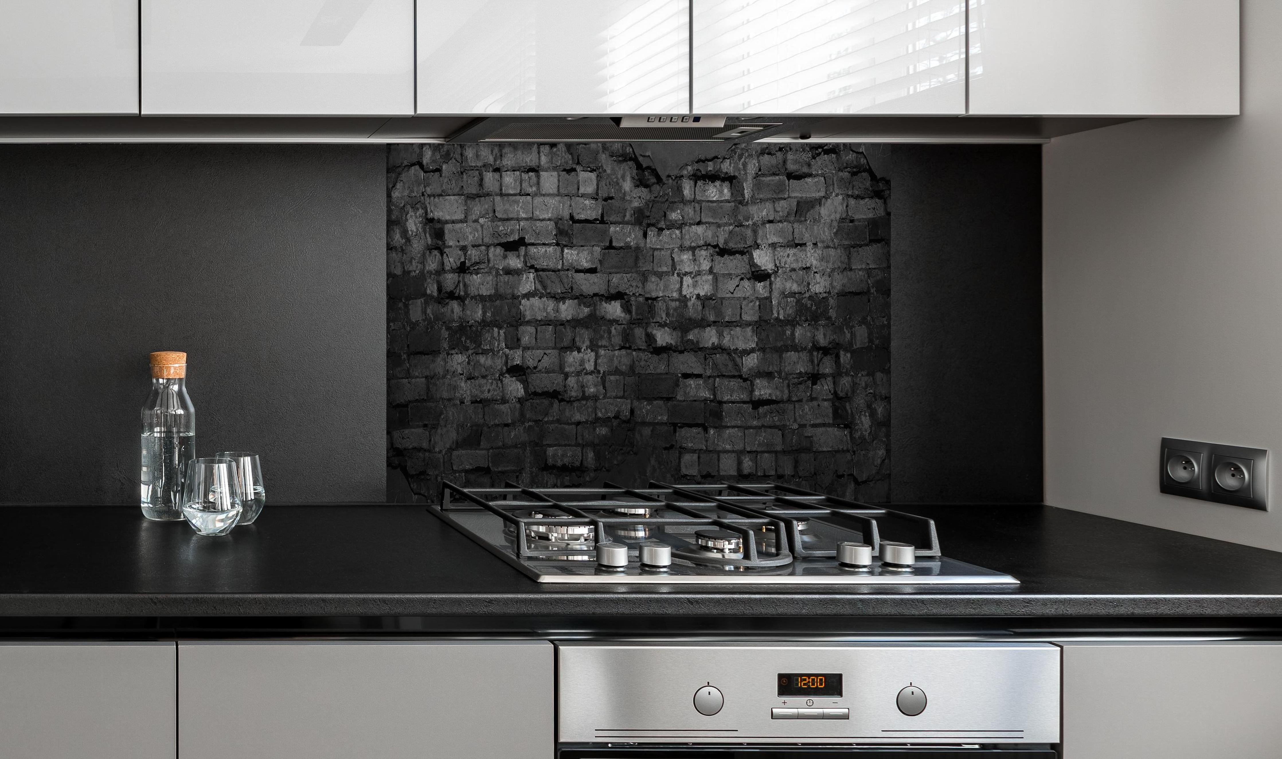 Spritzschutz - Schwarze alte Backsteinmauer hinter einem Cerankochfeld zwischen Holz-Kochutensilien
