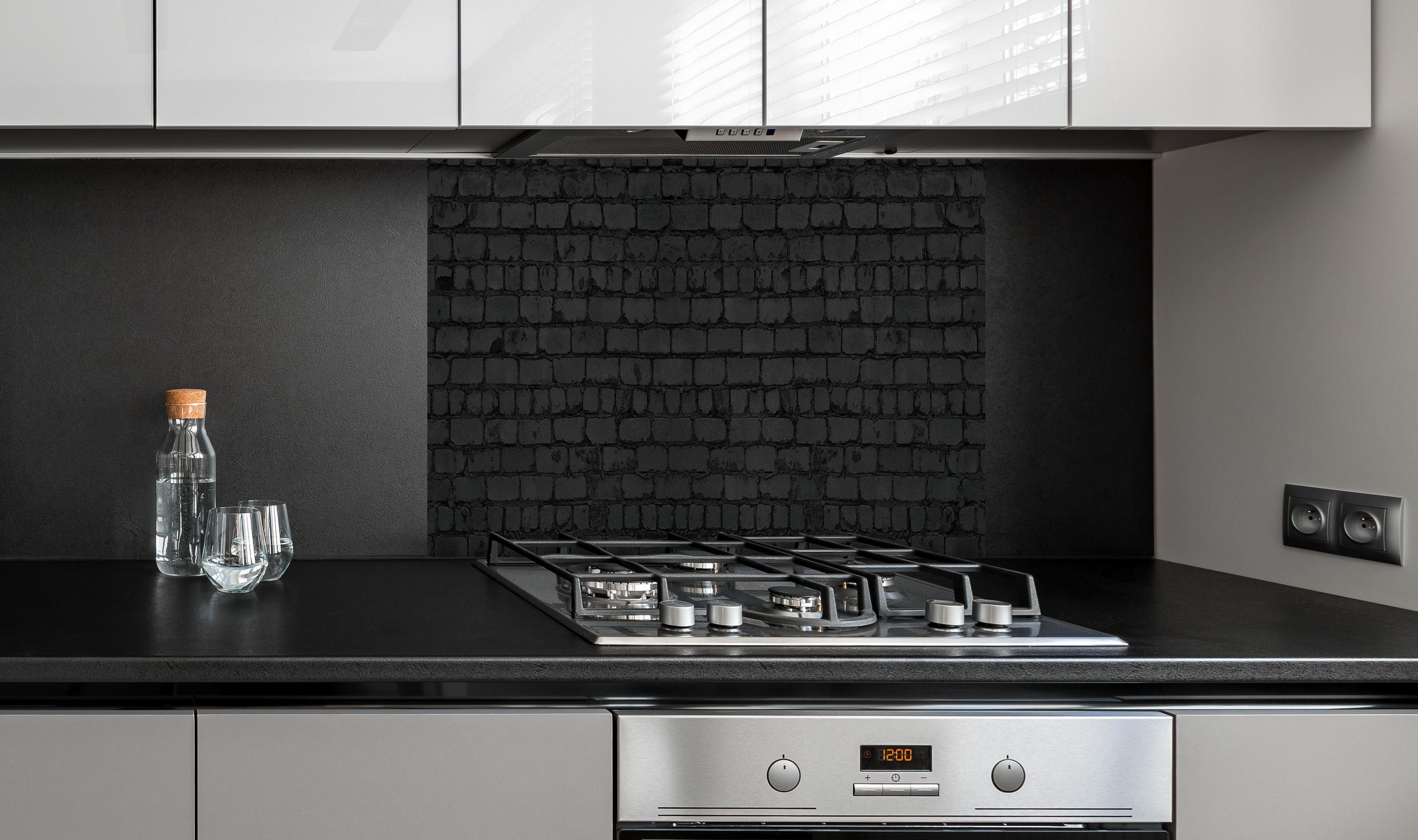 Spritzschutz - Schwarze raue Backsteinmauer hinter einem Cerankochfeld zwischen Holz-Kochutensilien
