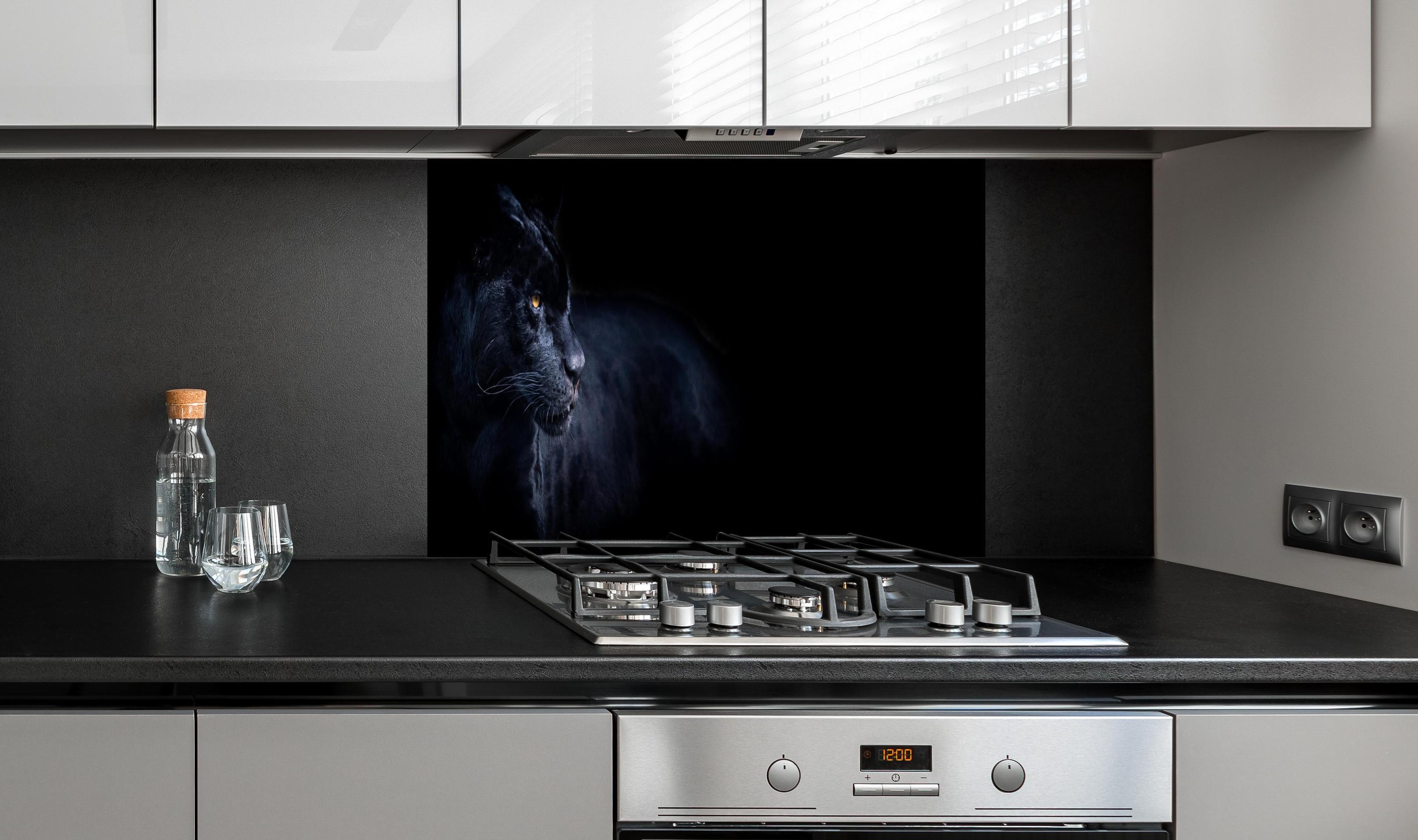Spritzschutz - Schwarzen Panther mit schwarzem Hintergrund hinter einem Cerankochfeld zwischen Holz-Kochutensilien
