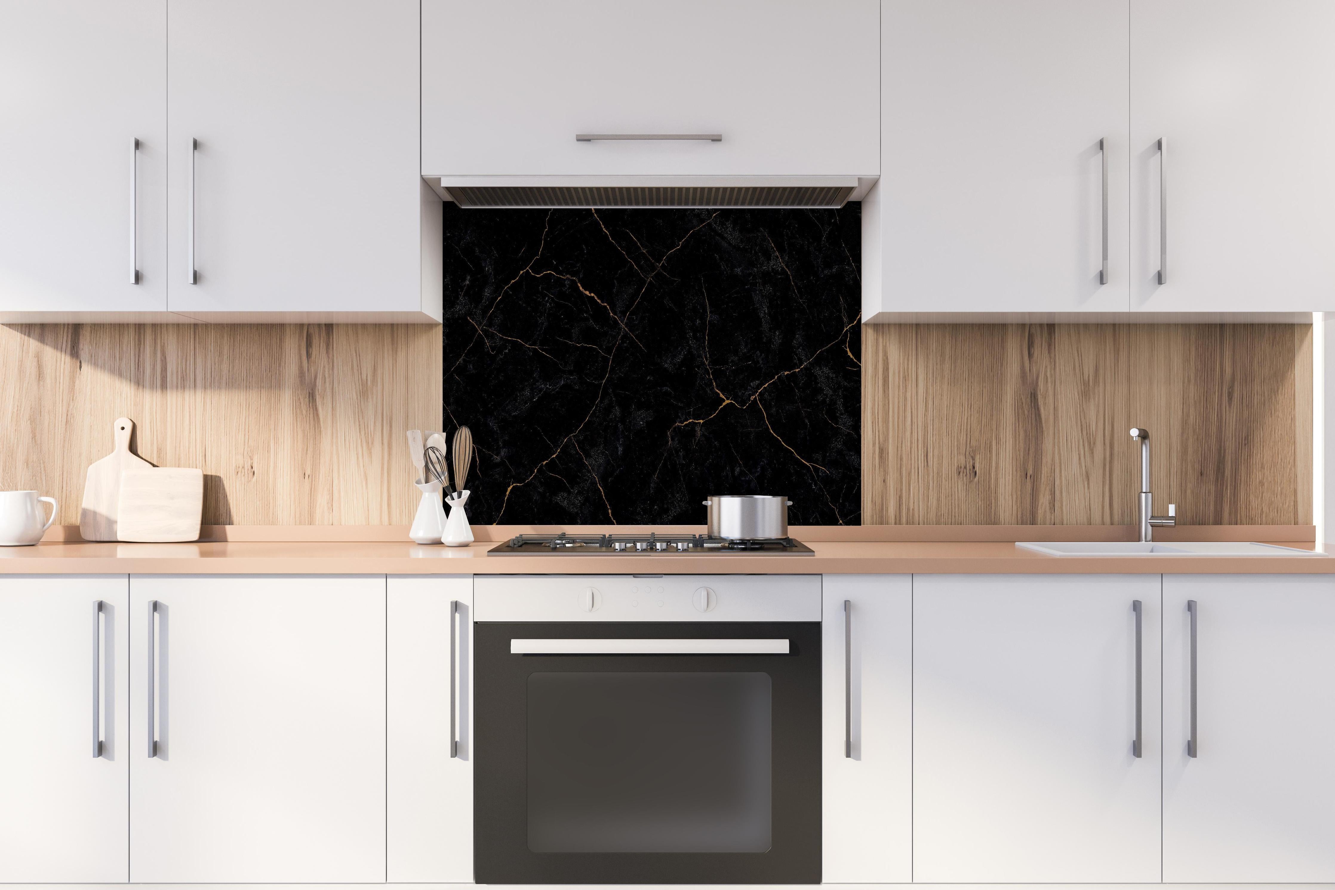 Spritzschutz - Schwarzer Marmor mit dünnen goldenen Adern hinter einem Cerankochfeld zwischen Holz-Kochutensilien
