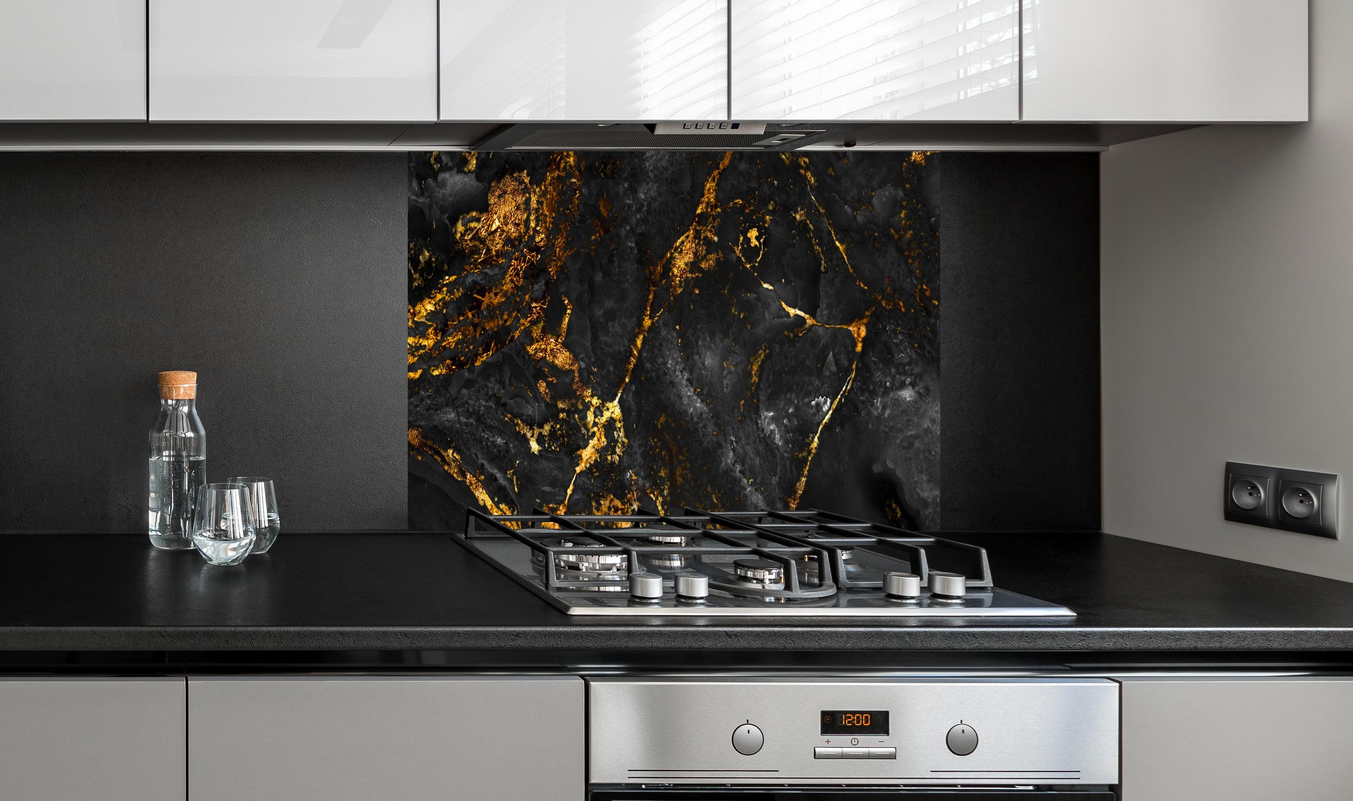 Spritzschutz - Schwarzer Marmor mit goldenen Adern hinter einem Cerankochfeld zwischen Holz-Kochutensilien
