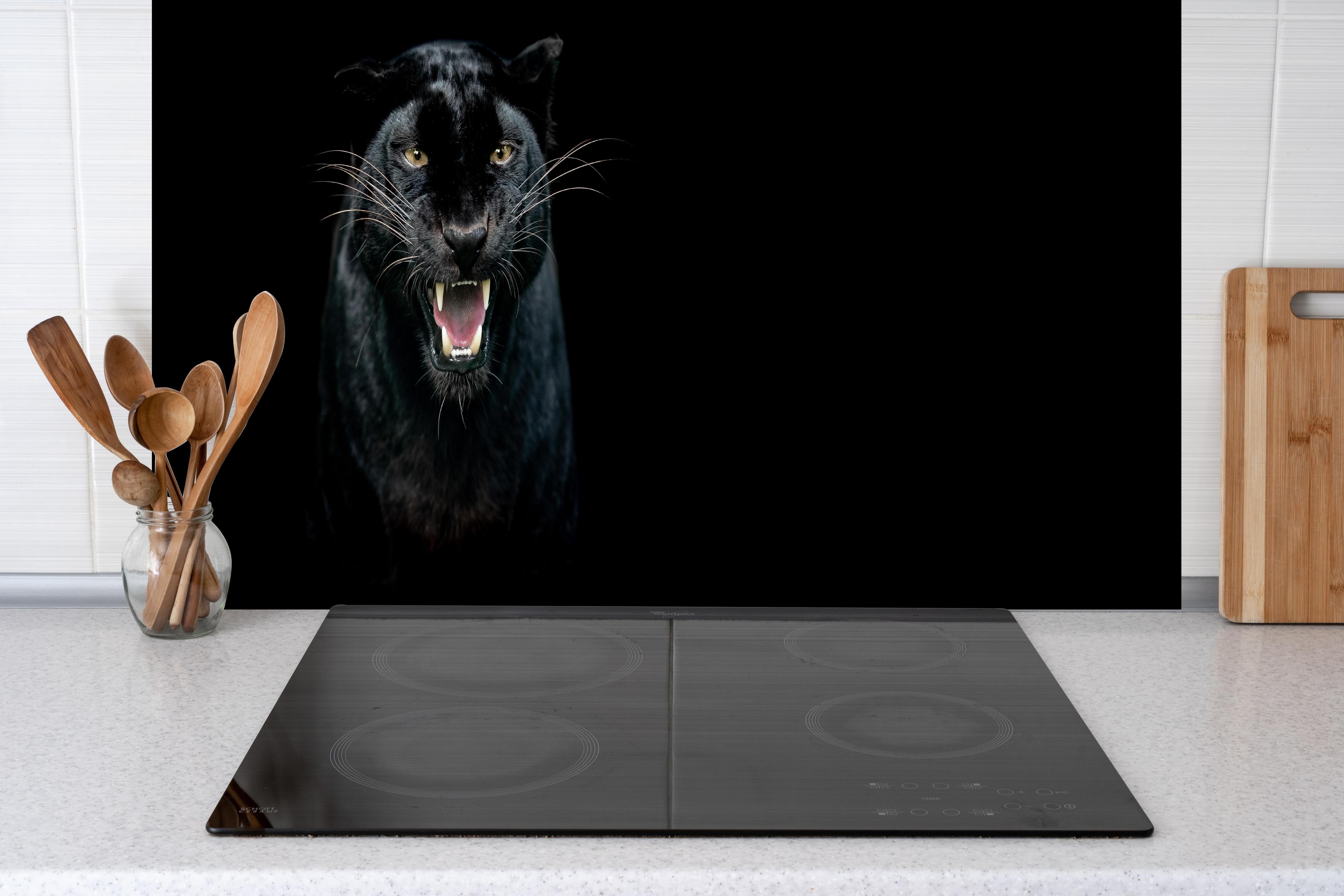 Spritzschutz - Schwarzer Panther auf schwarzem Hintergrund hinter einem Cerankochfeld zwischen Holz-Kochutensilien
