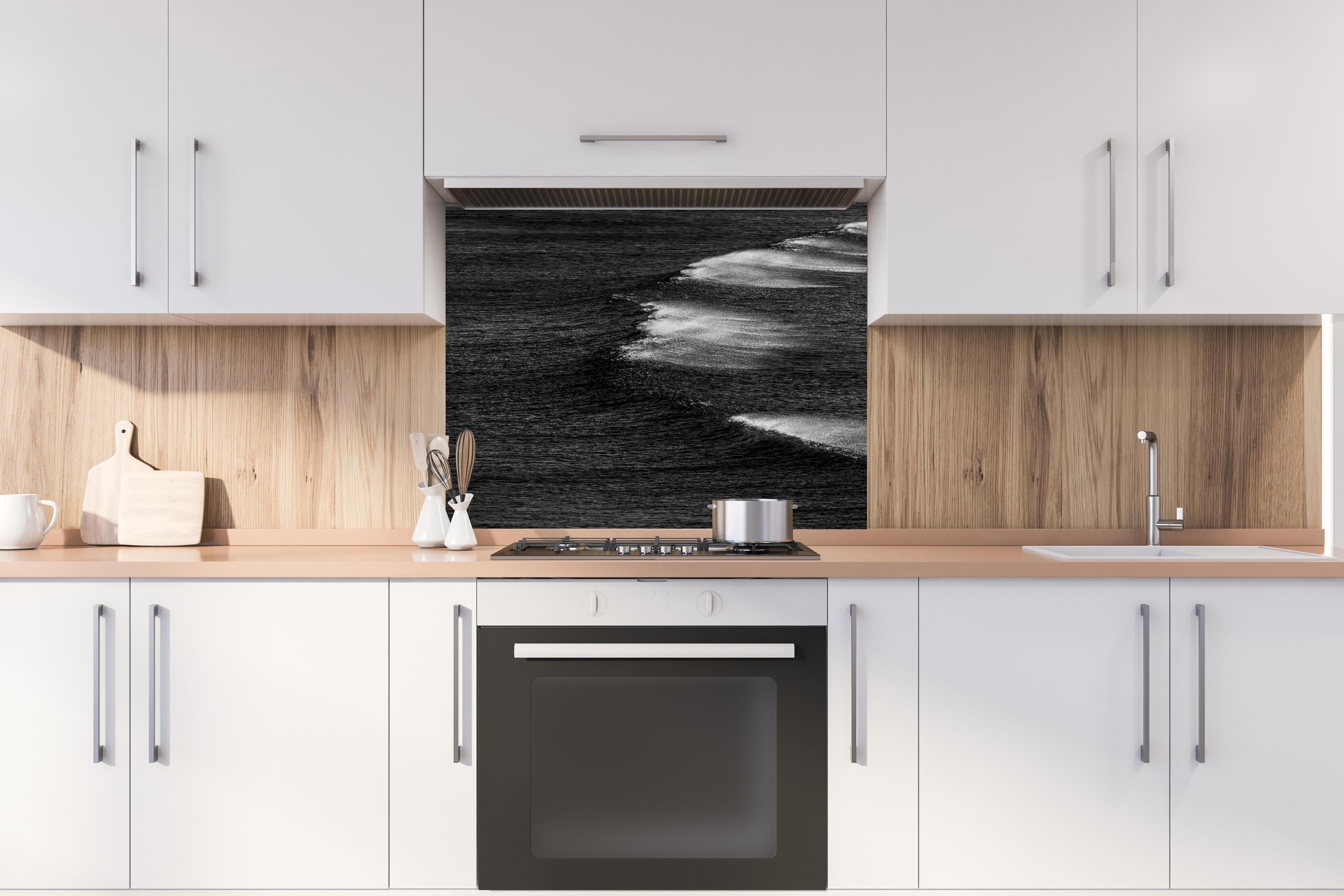Spritzschutz - Schwarzweiße Ozeanwellen aus der Vogelperspektive hinter einem Cerankochfeld zwischen Holz-Kochutensilien
