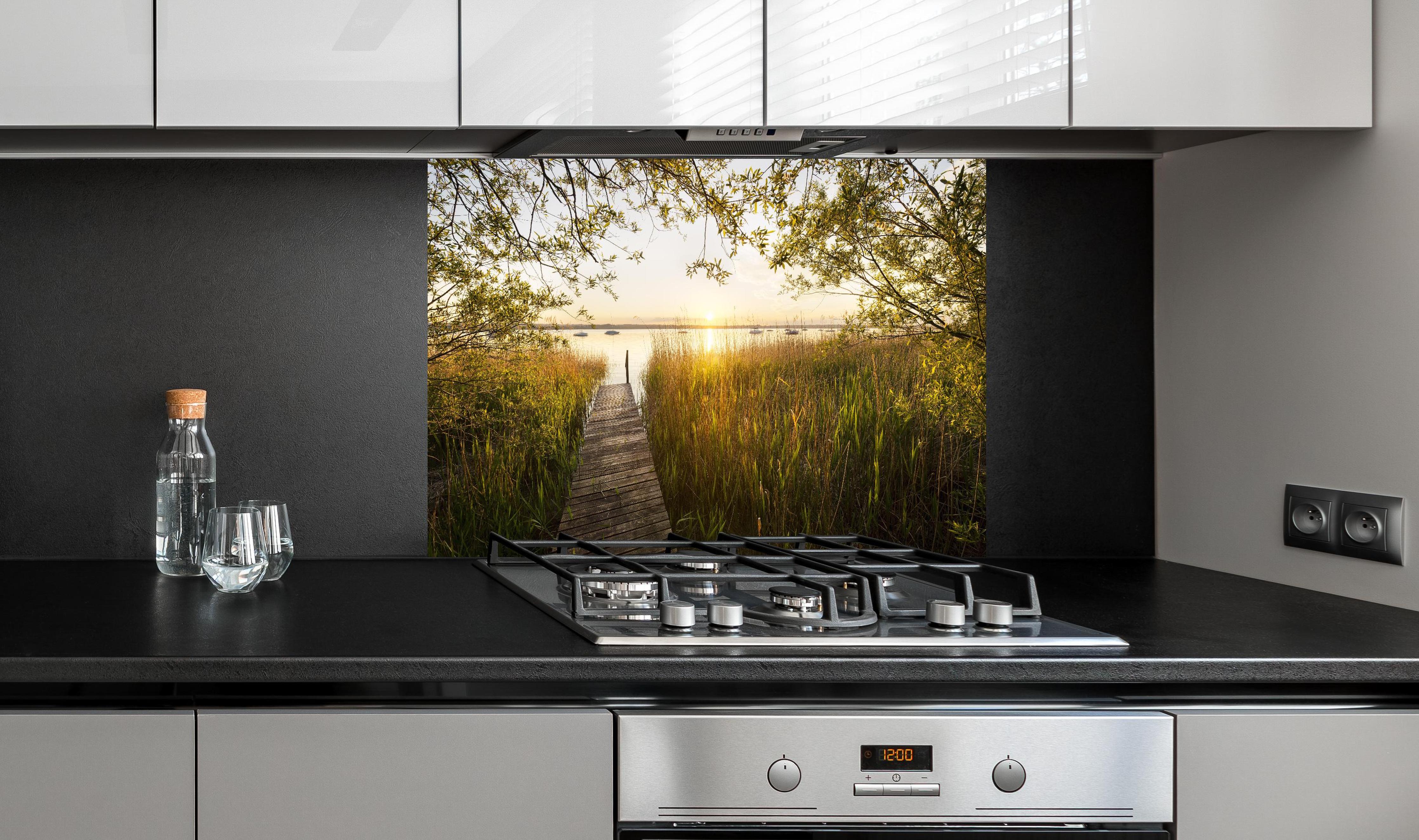 Spritzschutz - See in Bayern bei Sonnenuntergang hinter einem Cerankochfeld zwischen Holz-Kochutensilien
