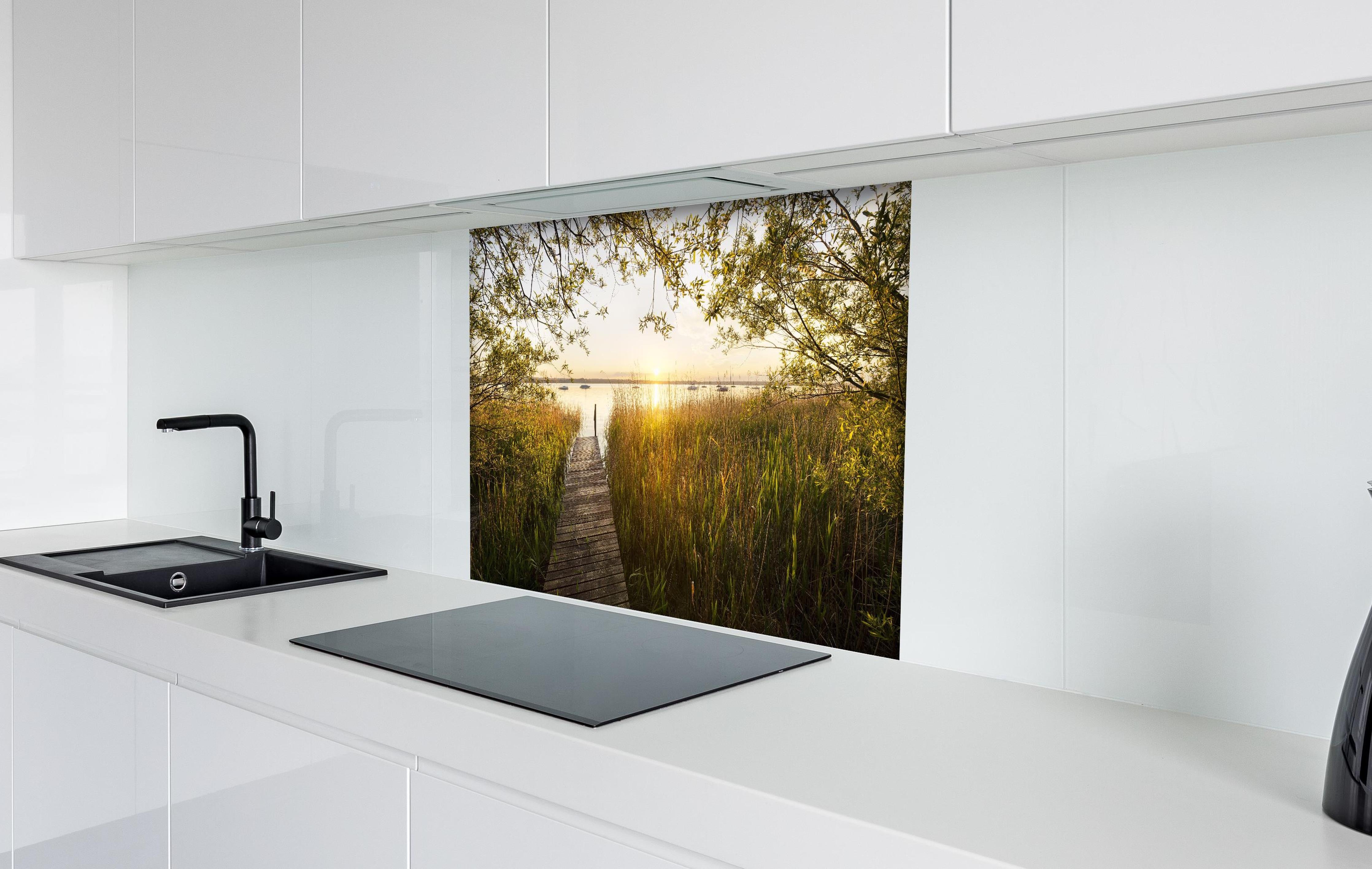 Spritzschutz - See in Bayern bei Sonnenuntergang hinter einem Cerankochfeld zwischen Holz-Kochutensilien
