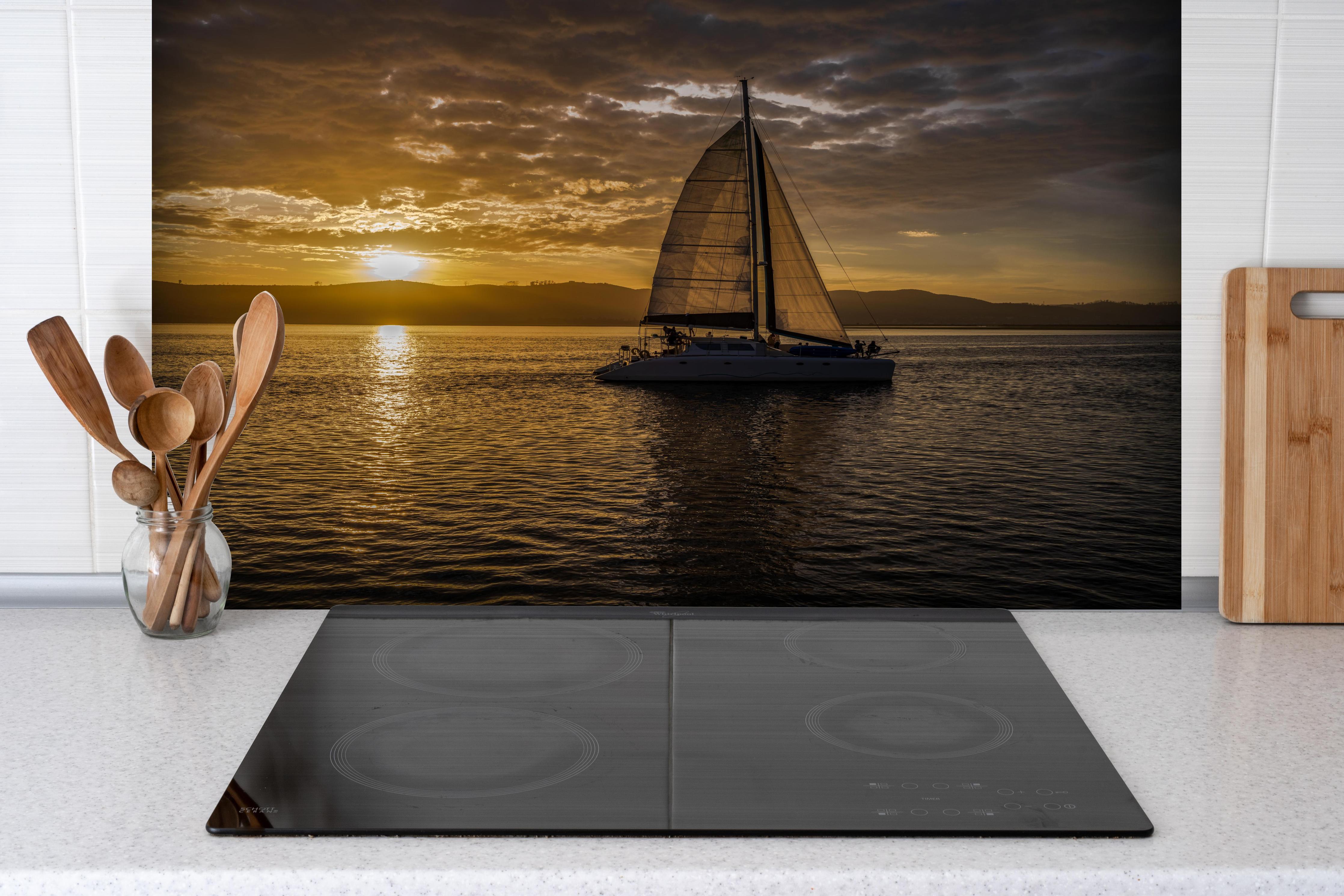 Spritzschutz - Segelboot bei Sonnenuntergang in der Lagune von Knysna hinter einem Cerankochfeld zwischen Holz-Kochutensilien
