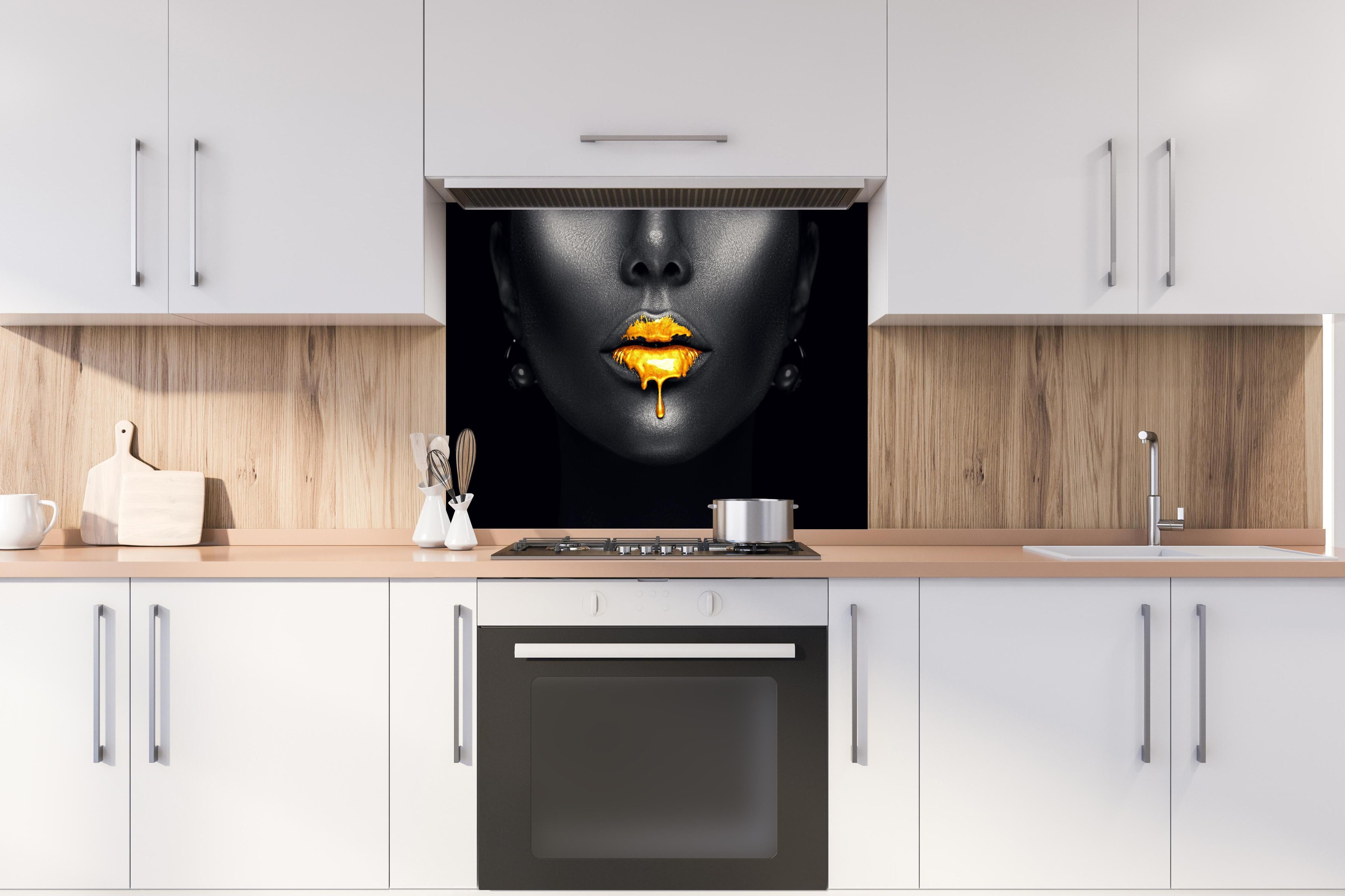Spritzschutz - Sinnliche Lippen mit Goldtropfen hinter einem Cerankochfeld zwischen Holz-Kochutensilien
