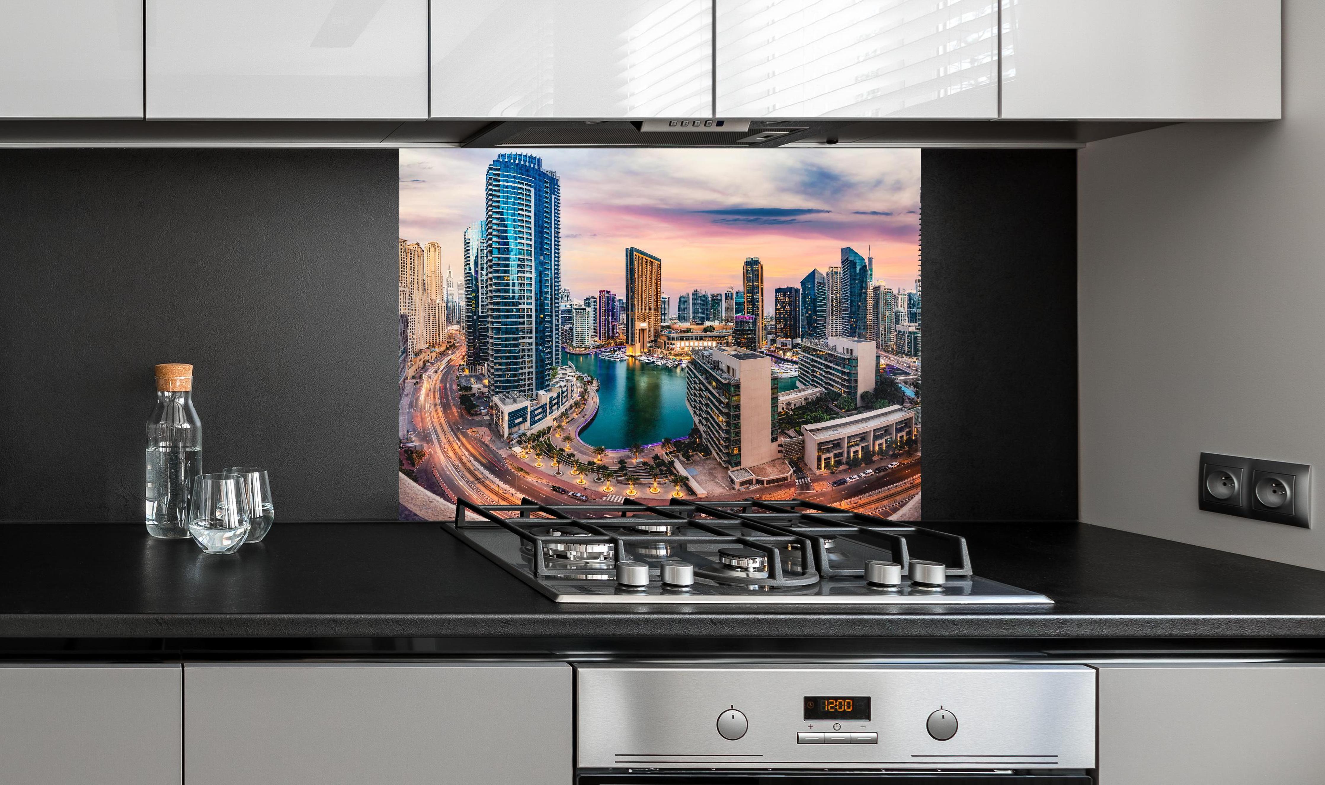 Spritzschutz - Skyline des Jachthafens von Dubai bei Sonnenuntergang hinter einem Cerankochfeld zwischen Holz-Kochutensilien
