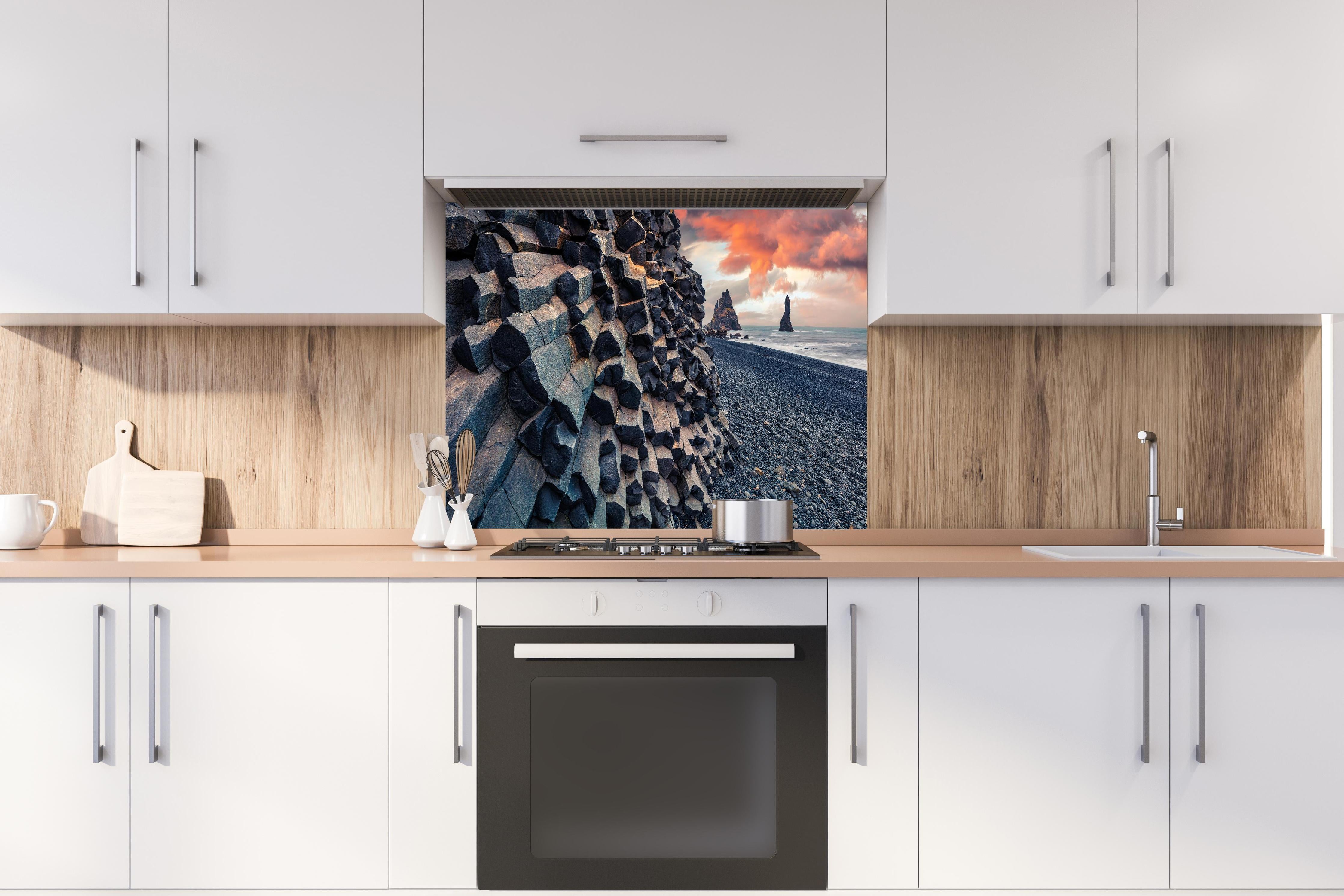 Spritzschutz - Sonnenuntergang - Reynisdrangar, Atlantischer Ozean hinter einem Cerankochfeld zwischen Holz-Kochutensilien

