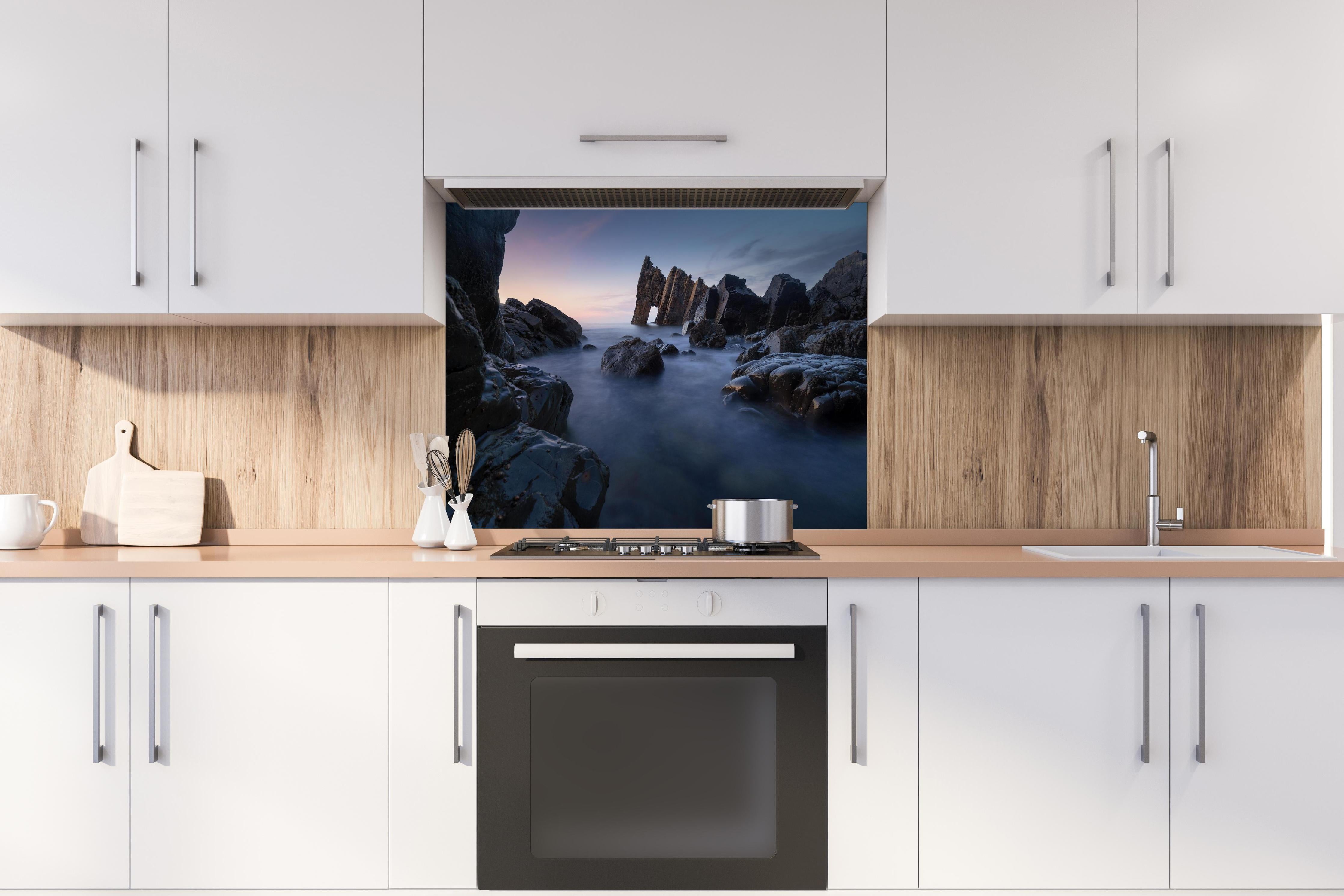 Spritzschutz - Sonnenuntergang am felsigen Meeresufer hinter einem Cerankochfeld zwischen Holz-Kochutensilien
