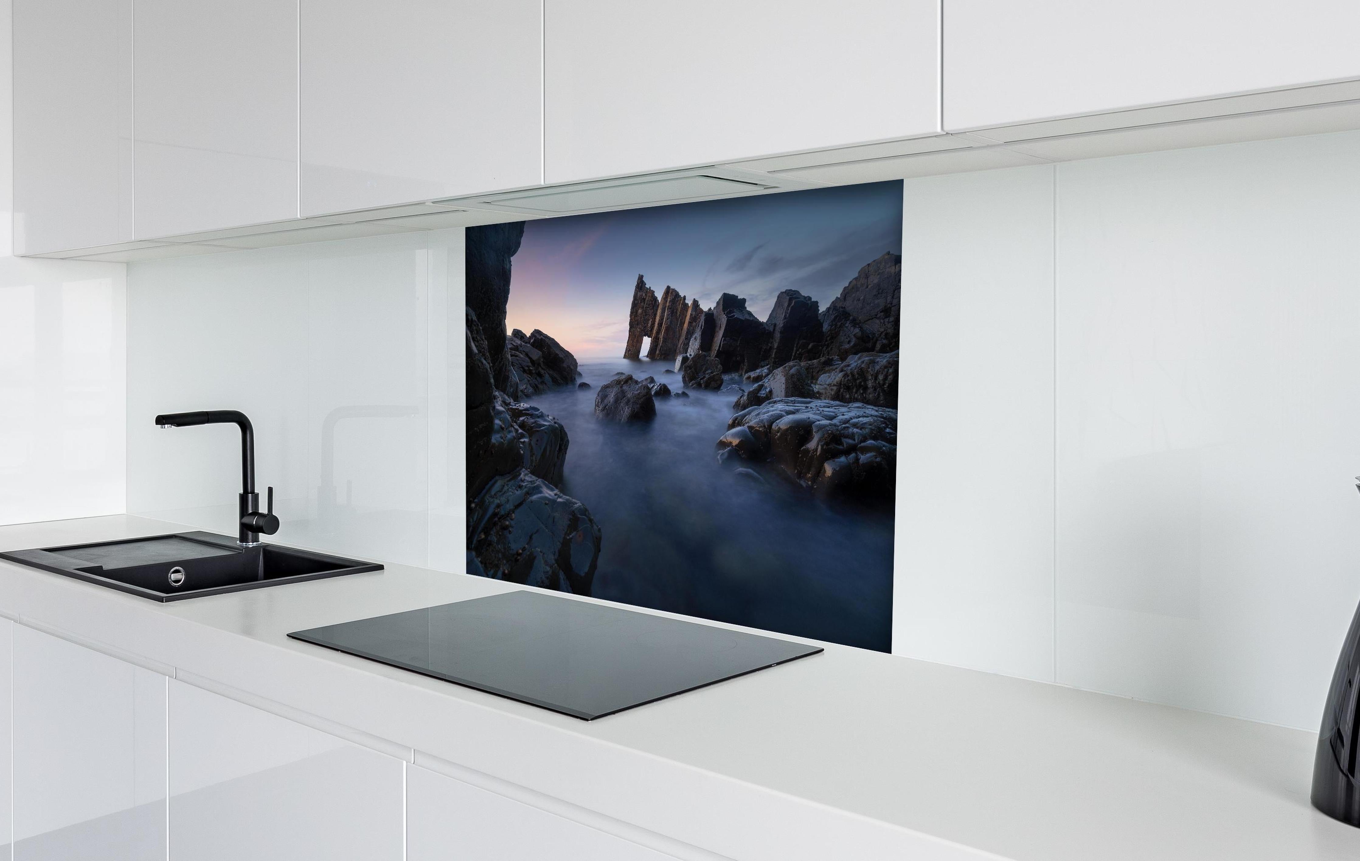 Spritzschutz - Sonnenuntergang am felsigen Meeresufer hinter einem Cerankochfeld zwischen Holz-Kochutensilien
