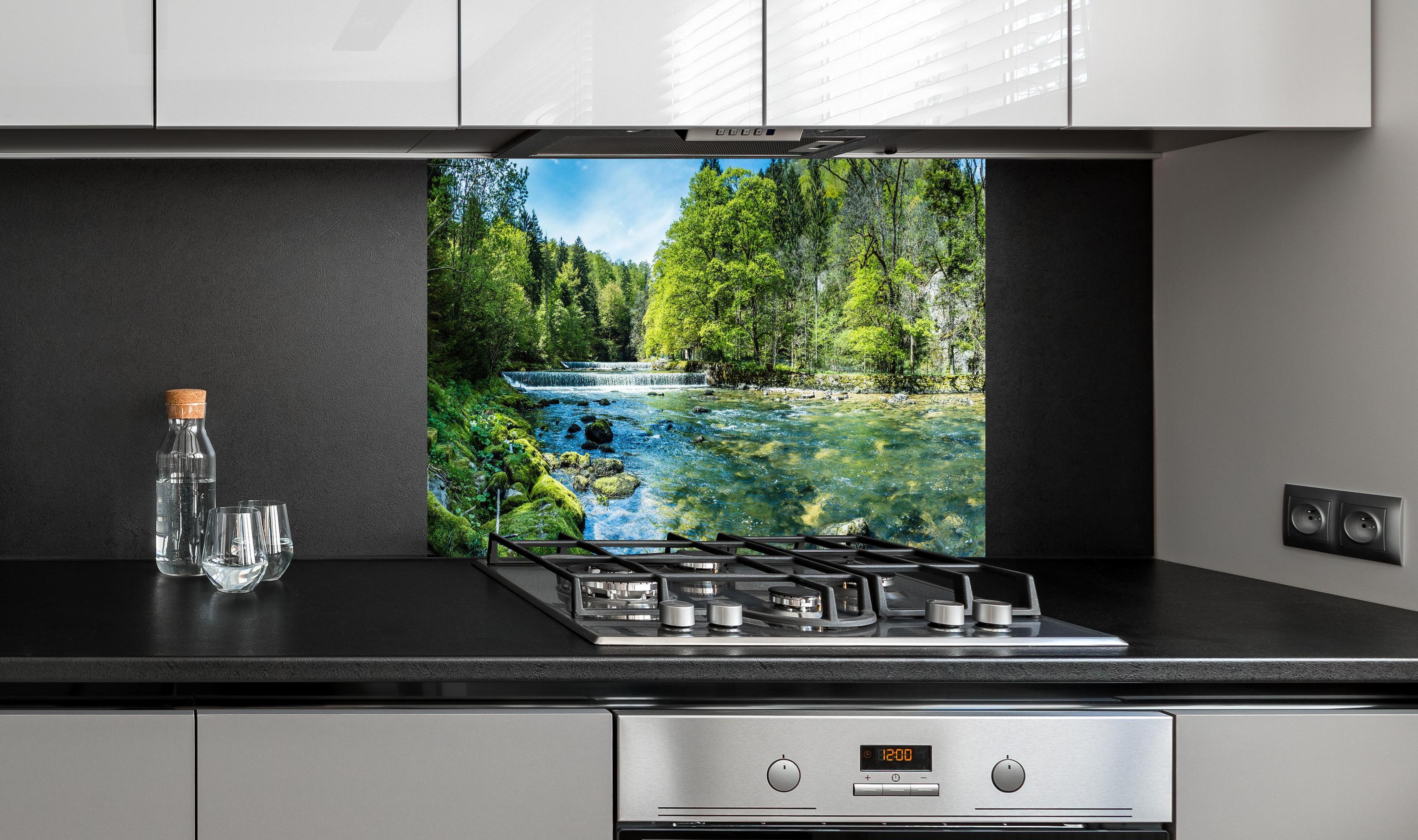 Spritzschutz - Sonnige Flusslandschaft in der Schweiz hinter einem Cerankochfeld zwischen Holz-Kochutensilien
