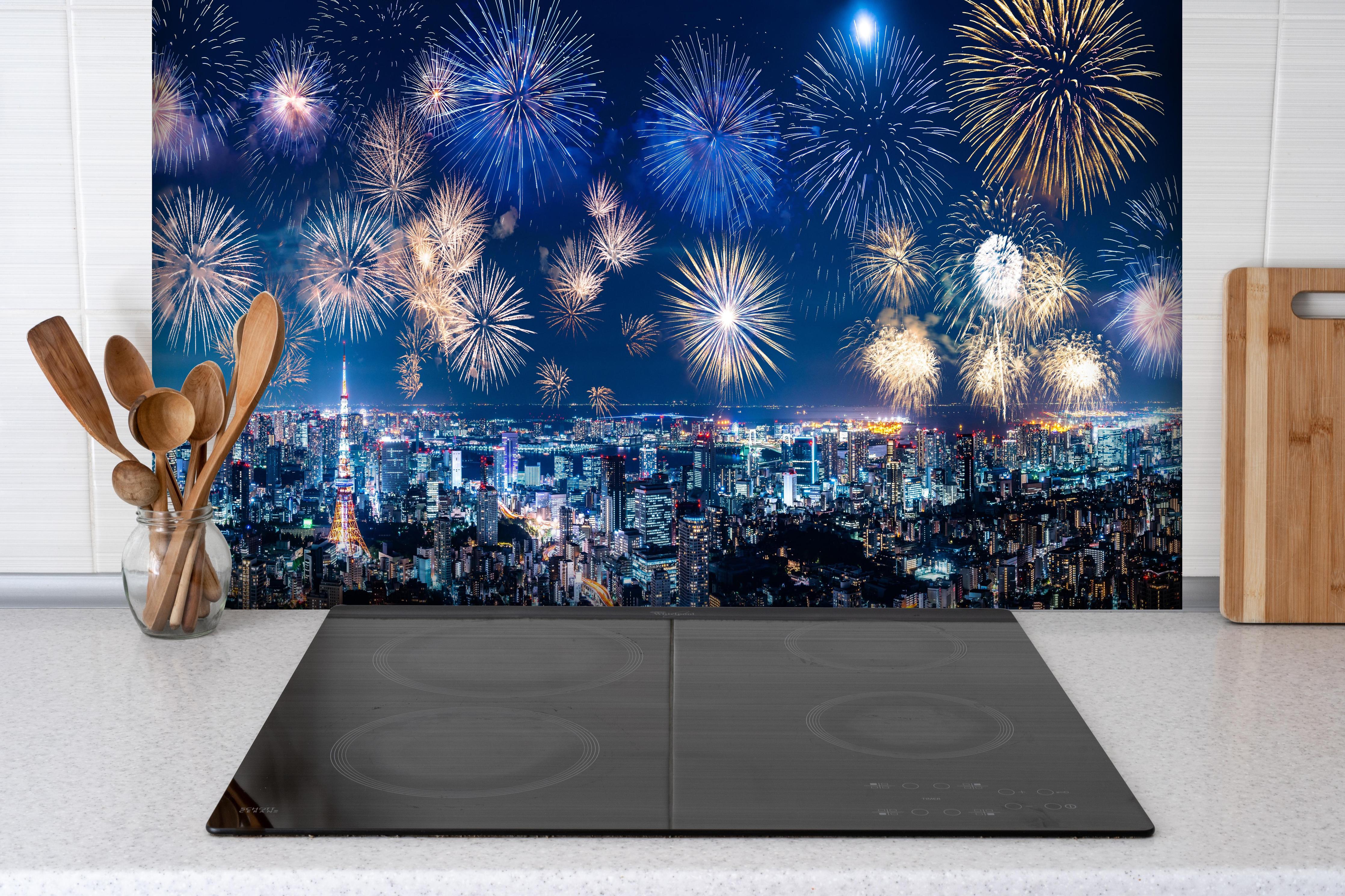 Spritzschutz - Spektakuläres Feuerwerk über Stadt bei Nacht hinter einem Cerankochfeld zwischen Holz-Kochutensilien
