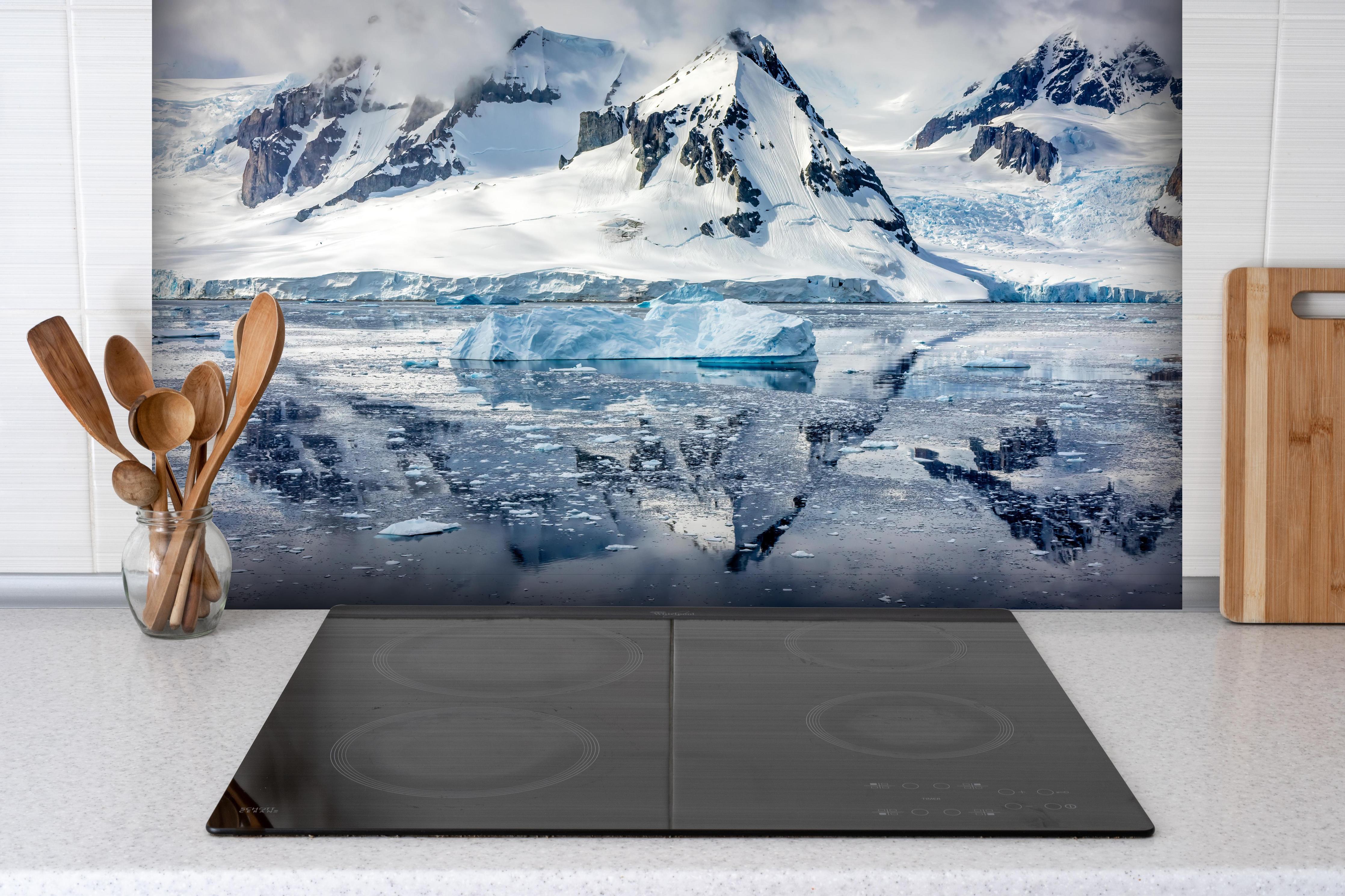 Spritzschutz - Spiegelung eines antarktischen Eisbergs hinter einem Cerankochfeld zwischen Holz-Kochutensilien
