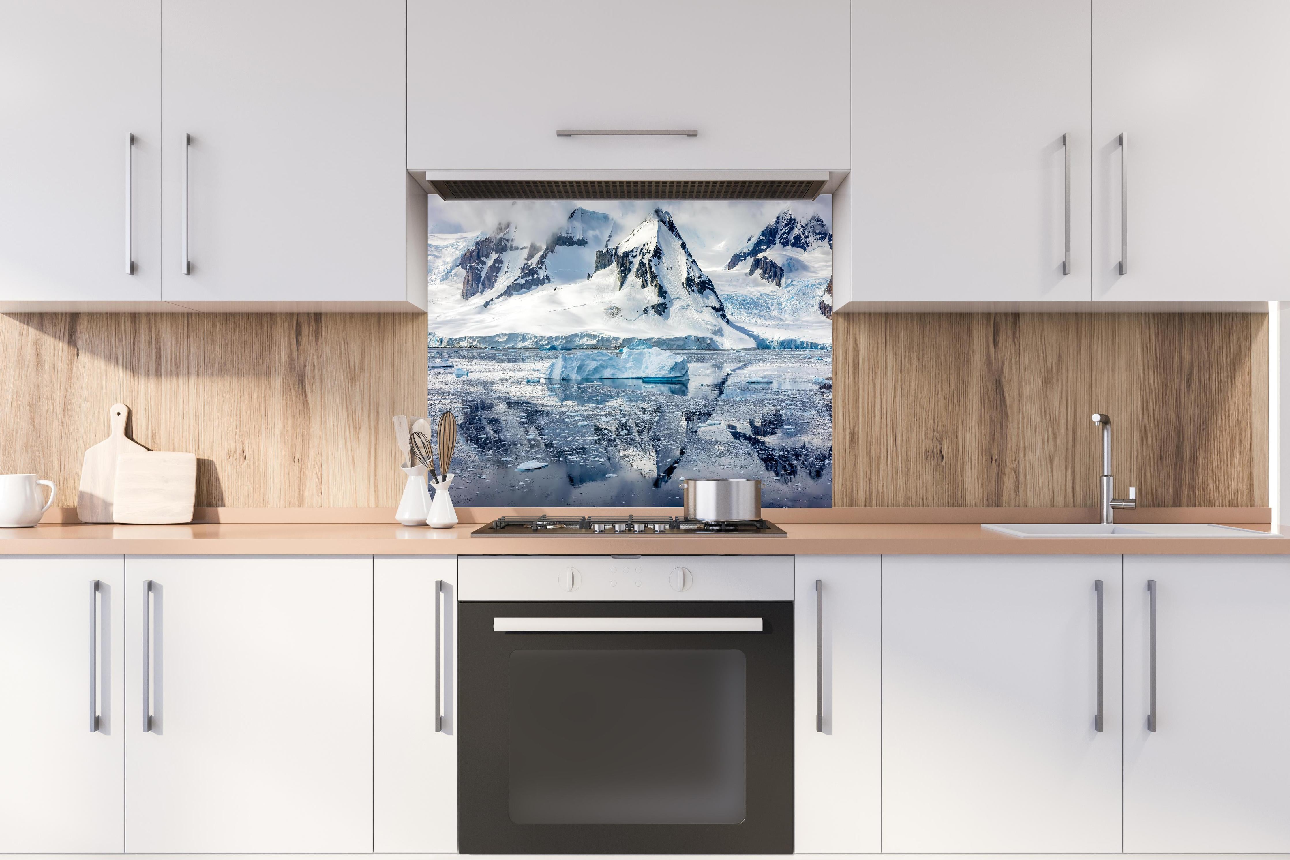 Spritzschutz - Spiegelung eines antarktischen Eisbergs hinter einem Cerankochfeld zwischen Holz-Kochutensilien
