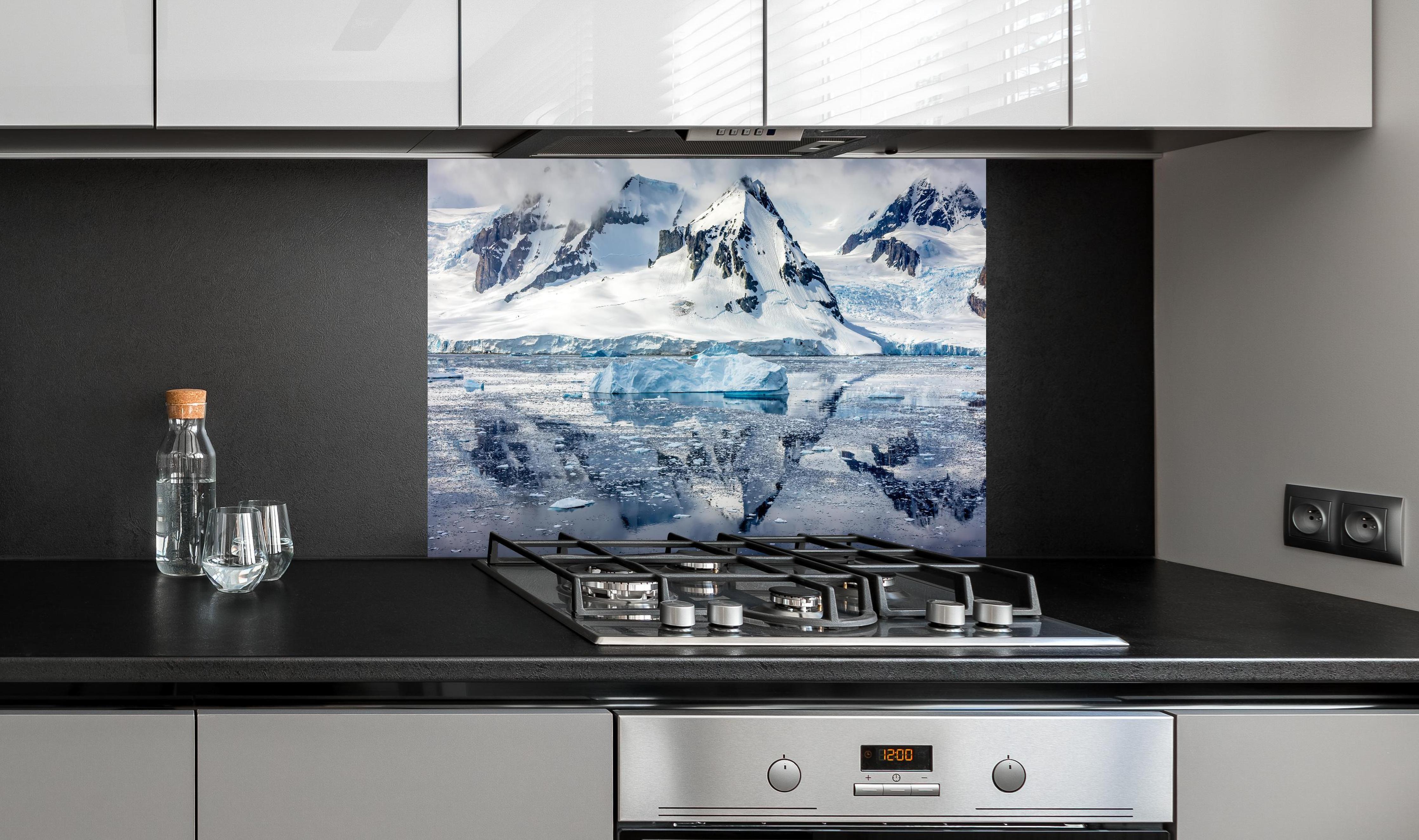 Spritzschutz - Spiegelung eines antarktischen Eisbergs hinter einem Cerankochfeld zwischen Holz-Kochutensilien
