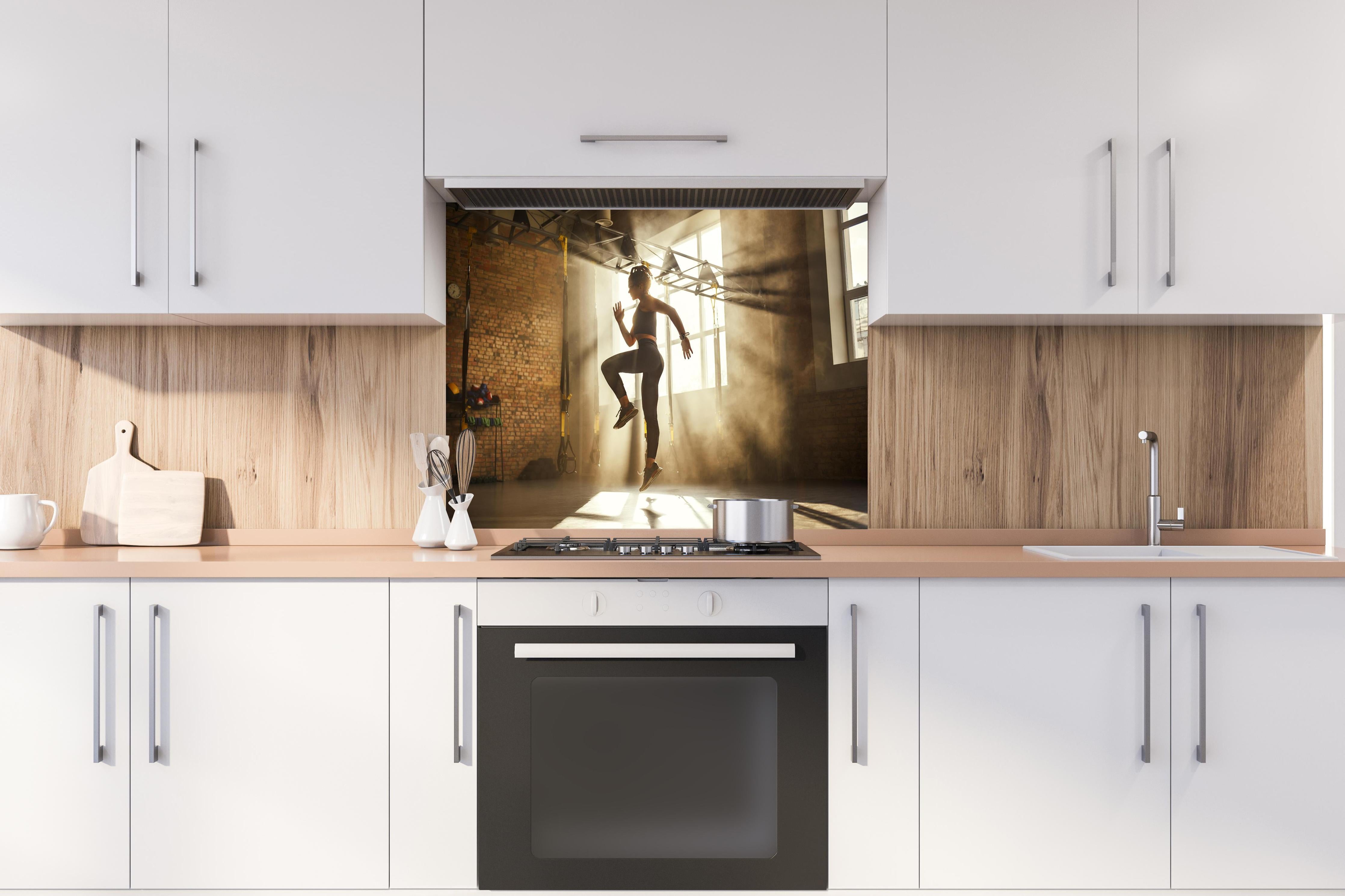 Spritzschutz - Sportlerin im Fitnesstudio hinter einem Cerankochfeld zwischen Holz-Kochutensilien
