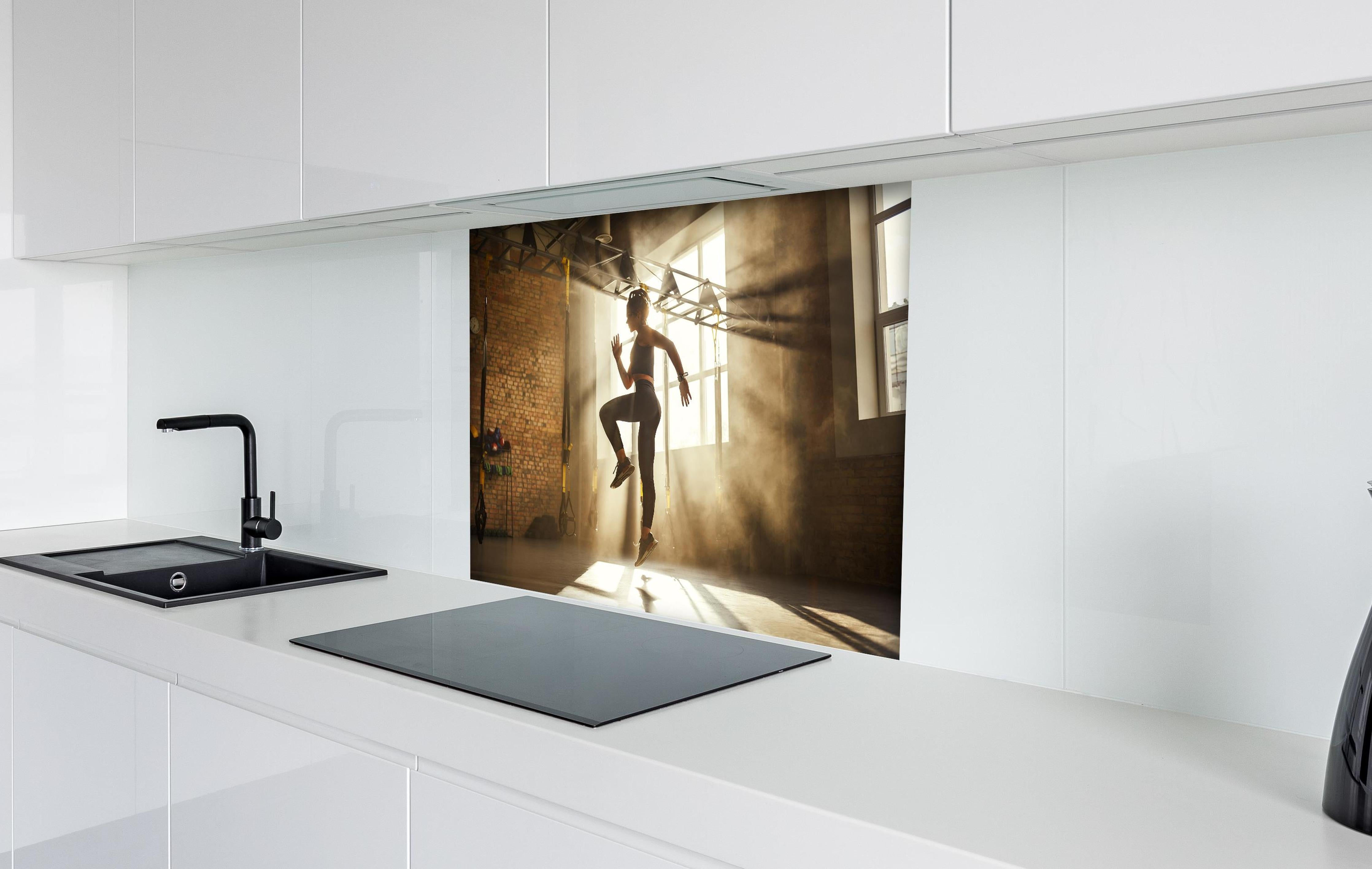 Spritzschutz - Sportlerin im Fitnesstudio hinter einem Cerankochfeld zwischen Holz-Kochutensilien
