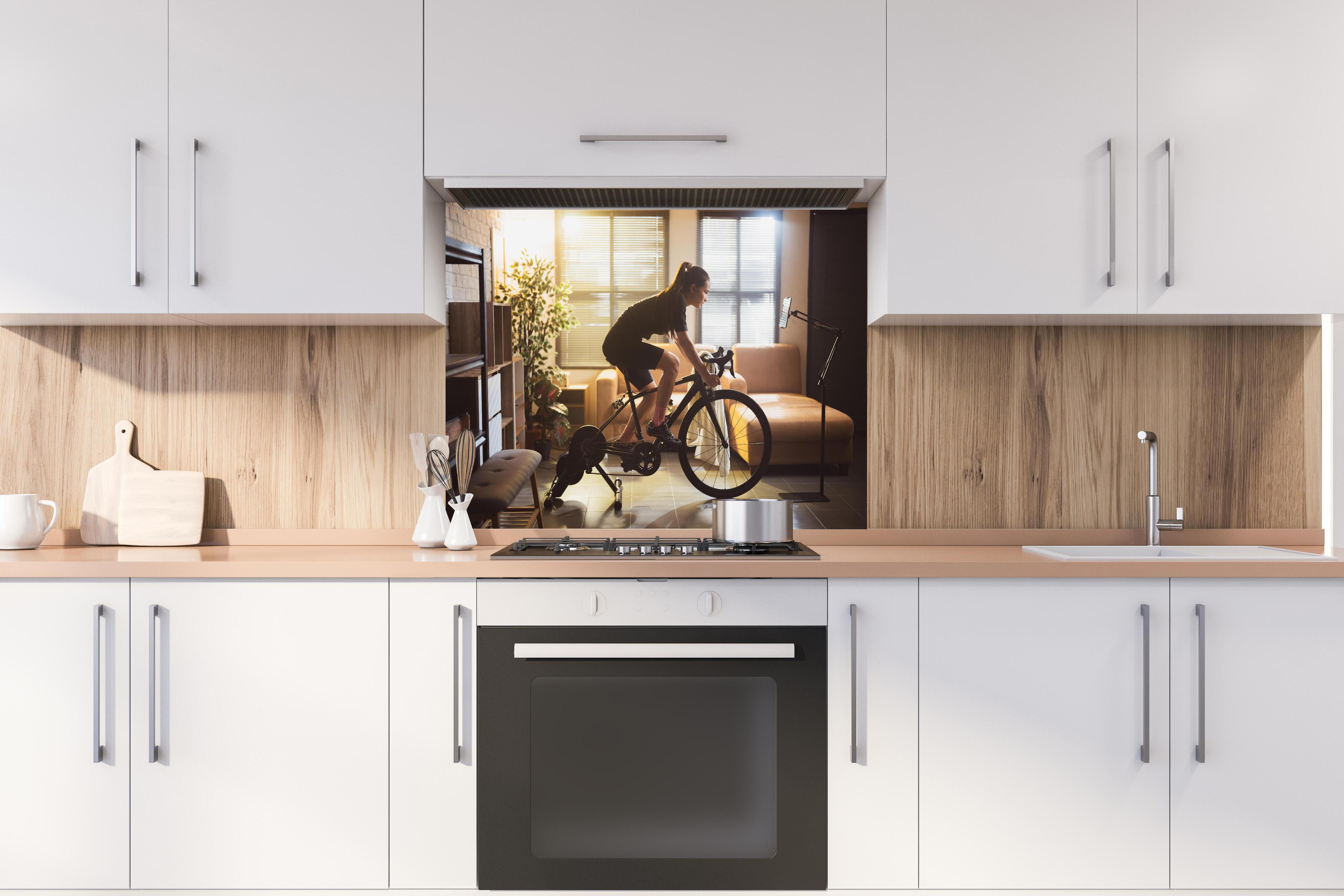 Spritzschutz - Sportliche Radfahrerin hinter einem Cerankochfeld zwischen Holz-Kochutensilien
