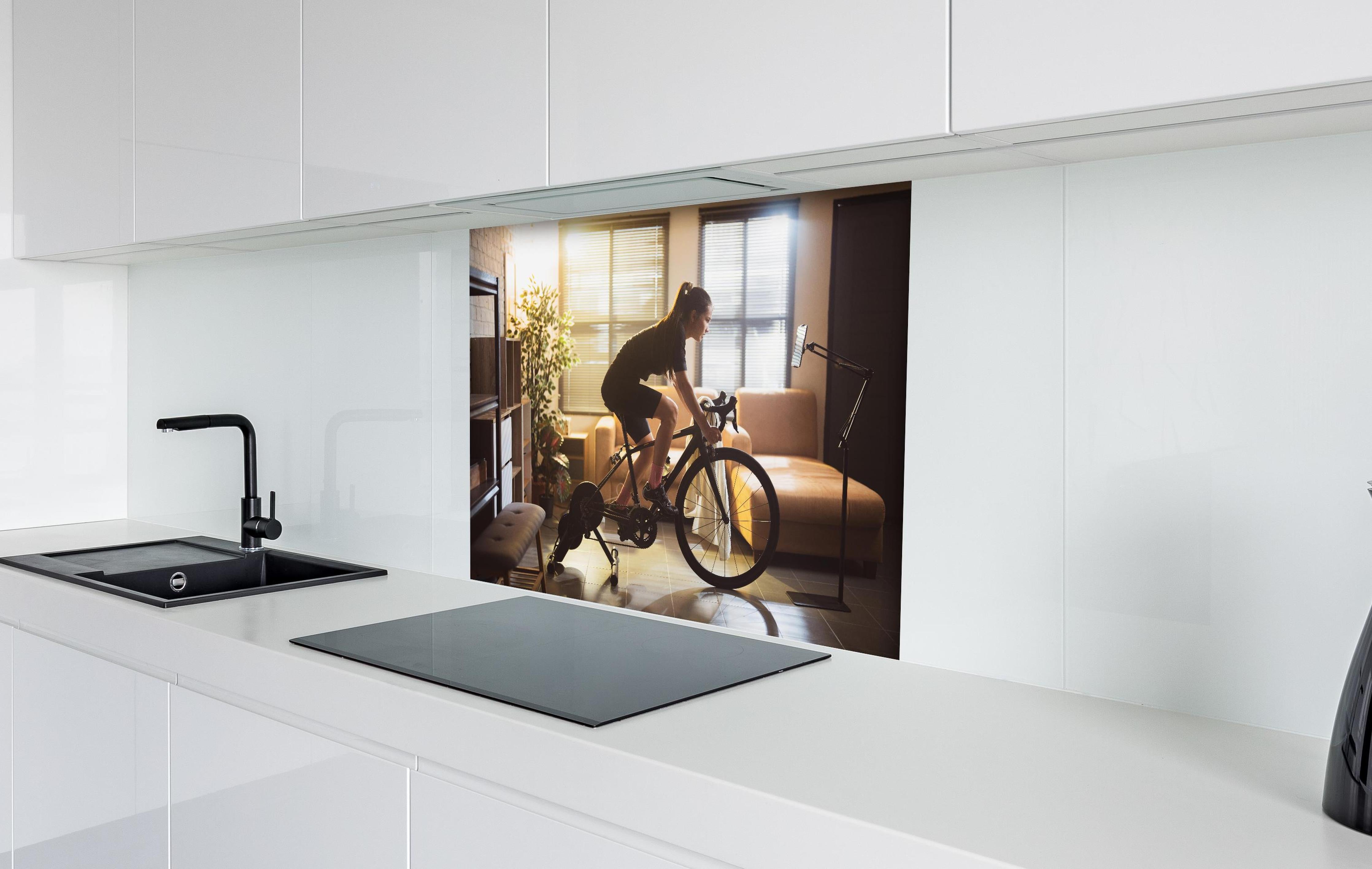 Spritzschutz - Sportliche Radfahrerin hinter einem Cerankochfeld zwischen Holz-Kochutensilien
