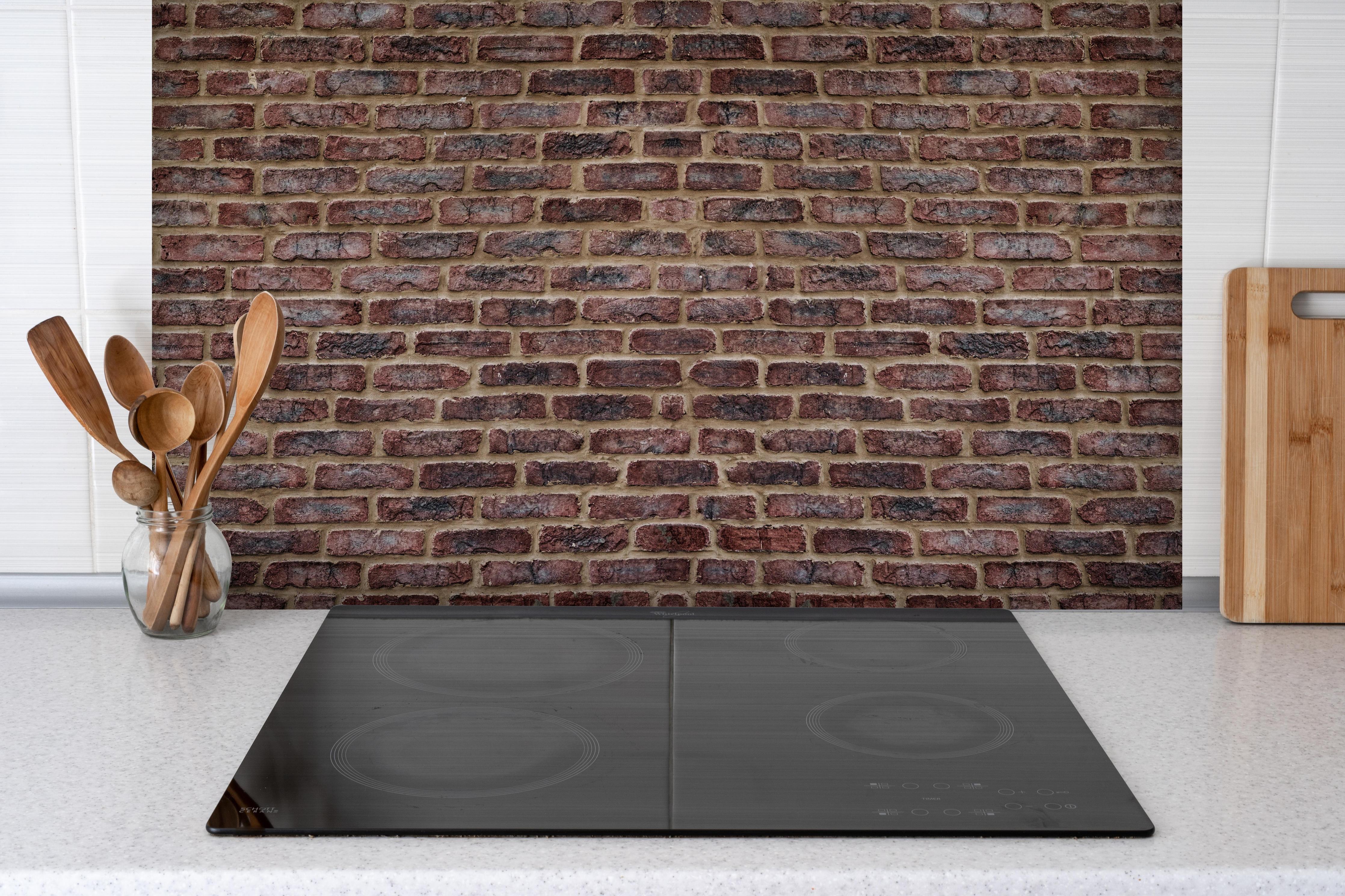 Spritzschutz - Alte rötliche Ziegelwand hinter einem Cerankochfeld zwischen Holz-Kochutensilien
