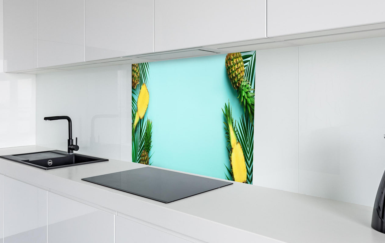 Spritzschutz - Ananas und tropische Palmenblätter  in weißer Hochglanz-Küche hinter einem Cerankochfeld