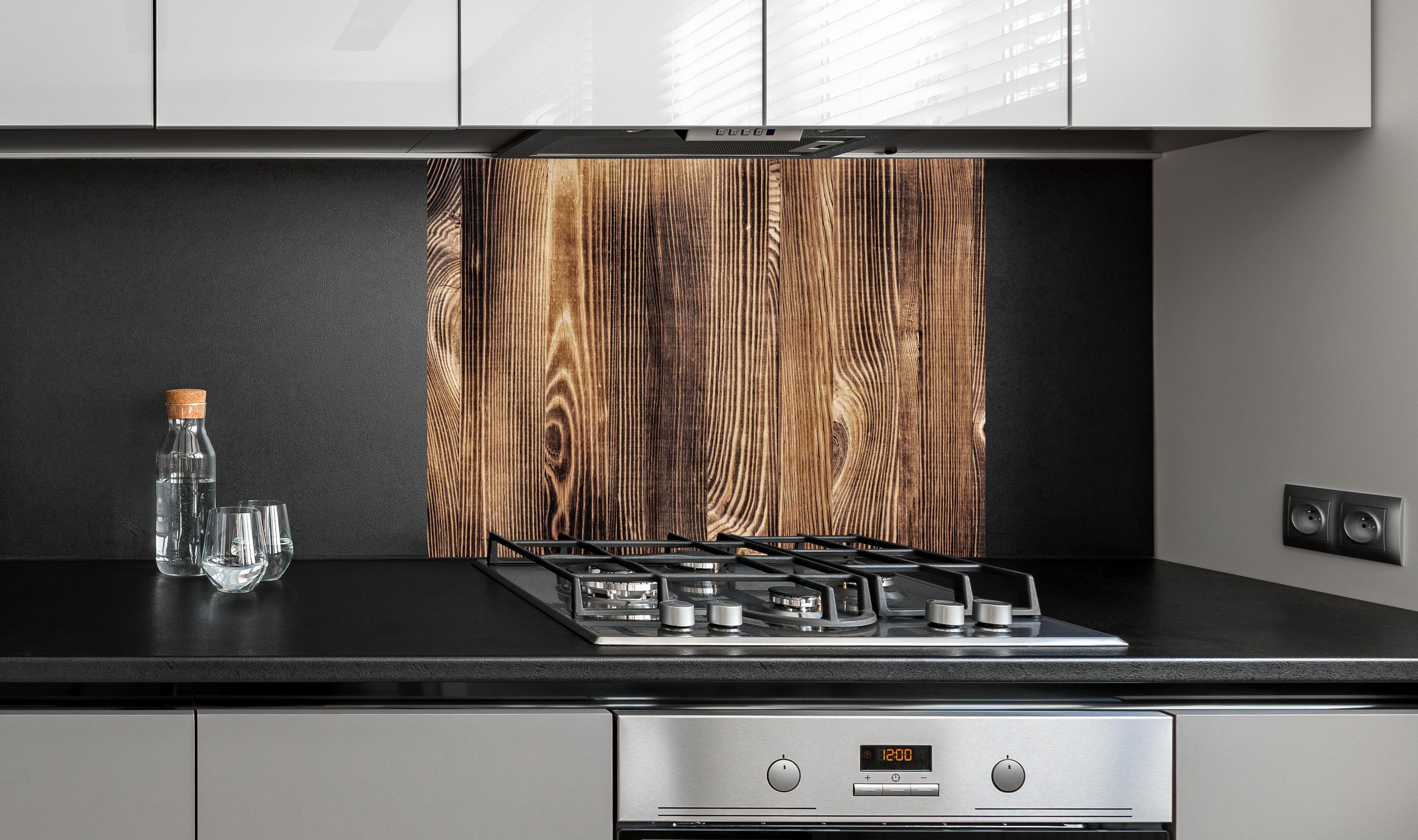 Spritzschutz - Angebrannte Naturholzplatte an edler Anthrazit-Wand hinter silbernem Gasherd