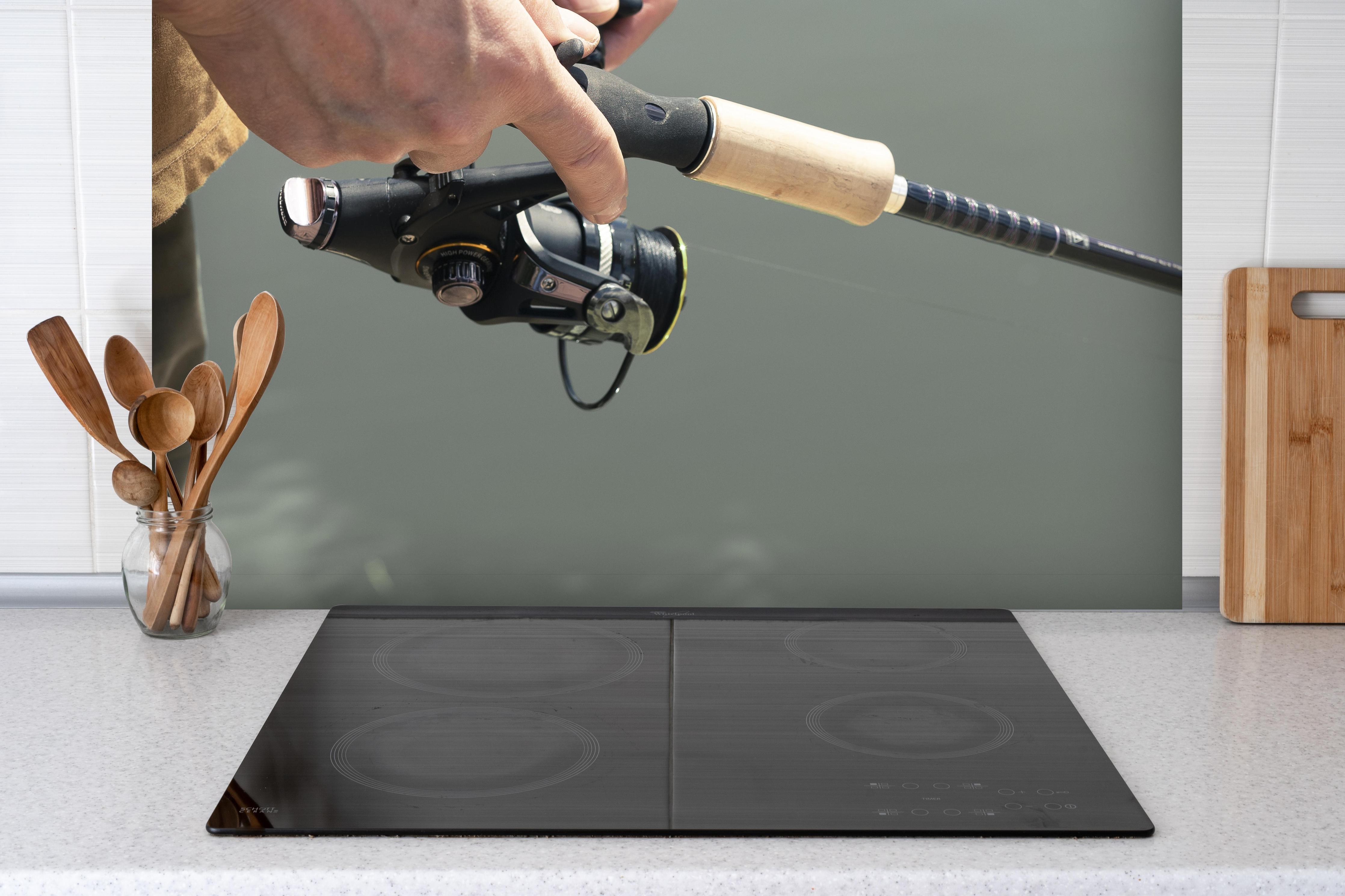 Spritzschutz - Angelroute beim Fischen - Nahaufnahme hinter einem Cerankochfeld zwischen Holz-Kochutensilien
