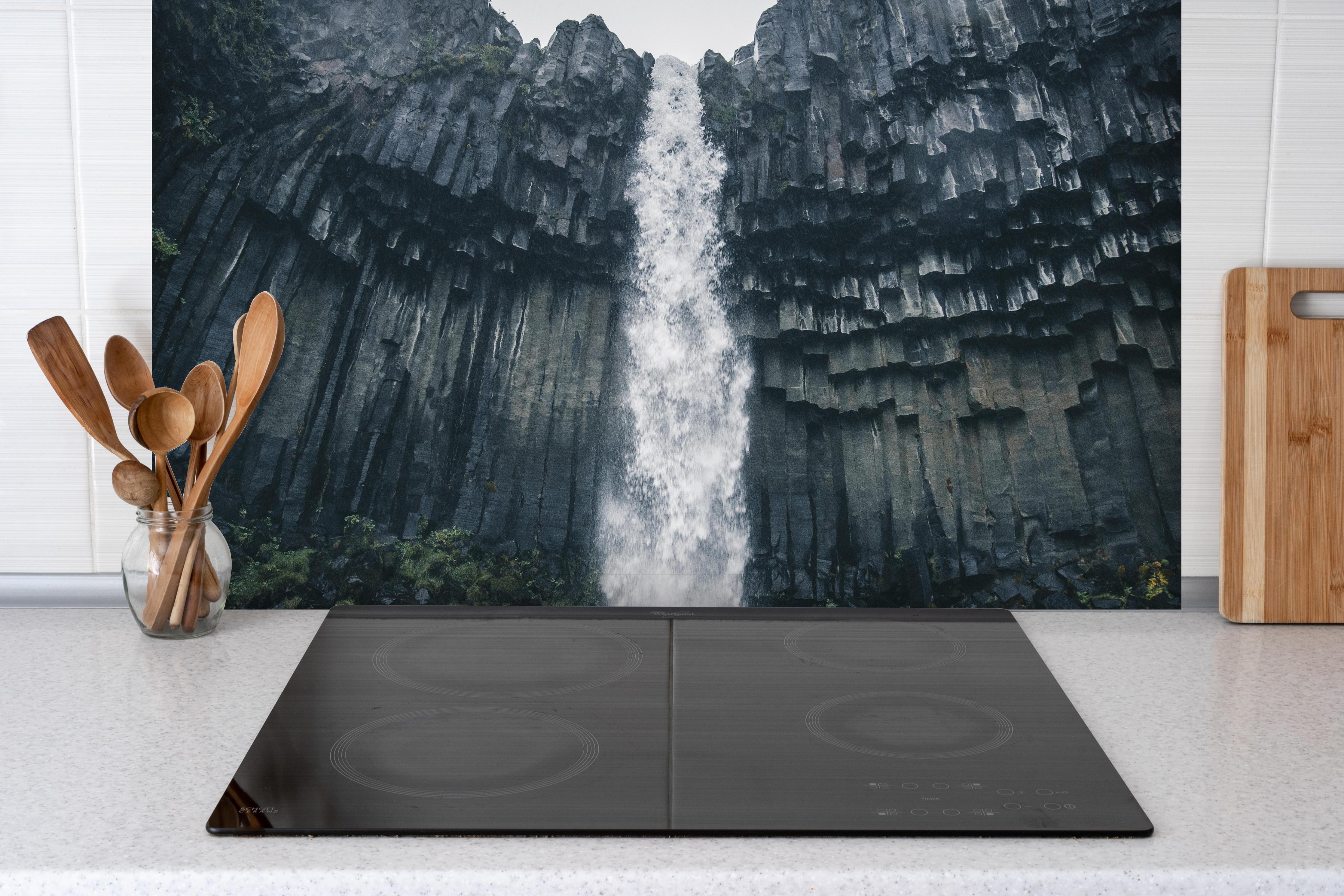 Spritzschutz - Beeindruckender Svartifoss Wasserfall hinter einem Cerankochfeld zwischen Holz-Kochutensilien
