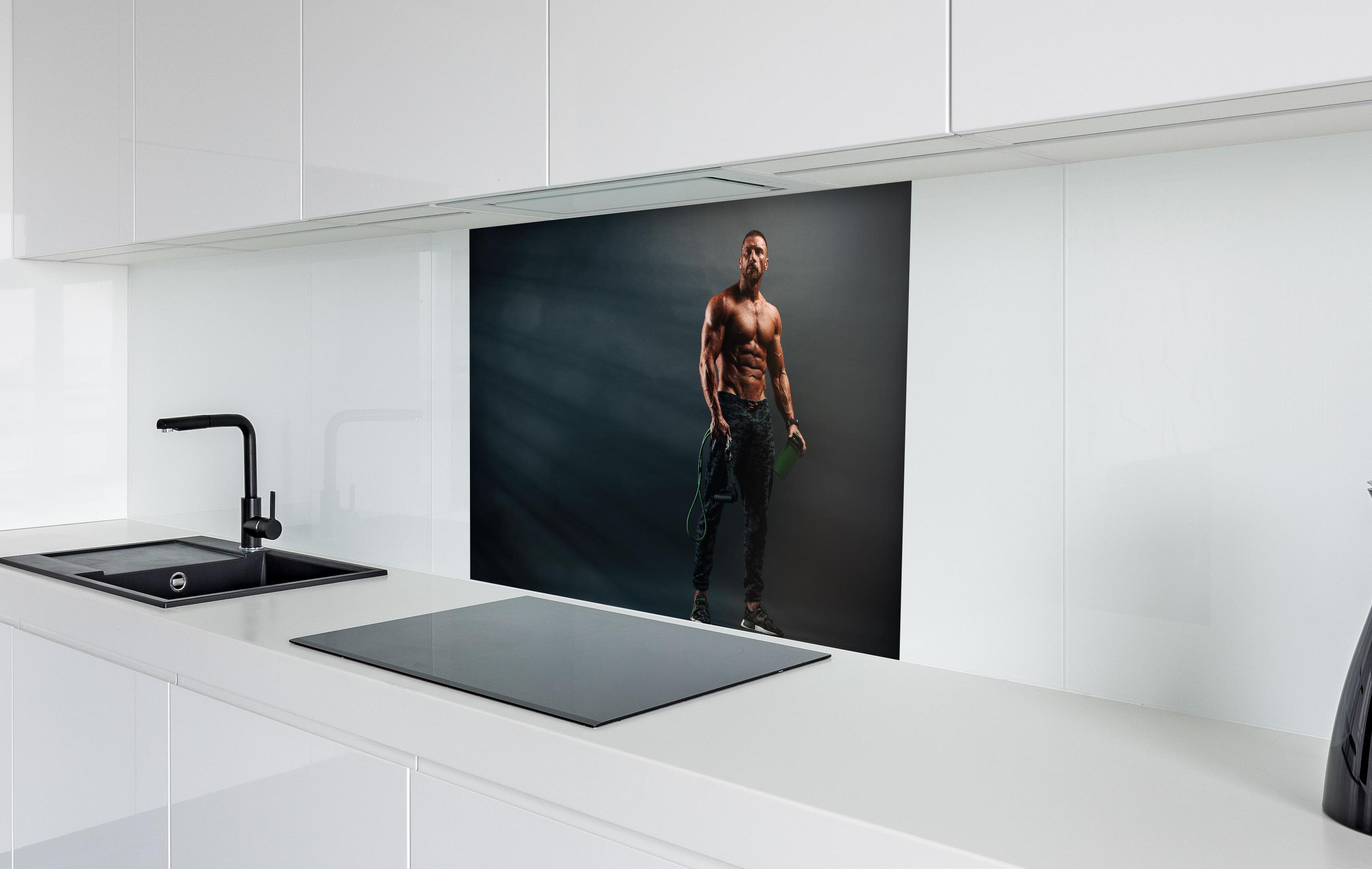 Spritzschutz - Bodybuilder - Training  in weißer Hochglanz-Küche hinter einem Cerankochfeld