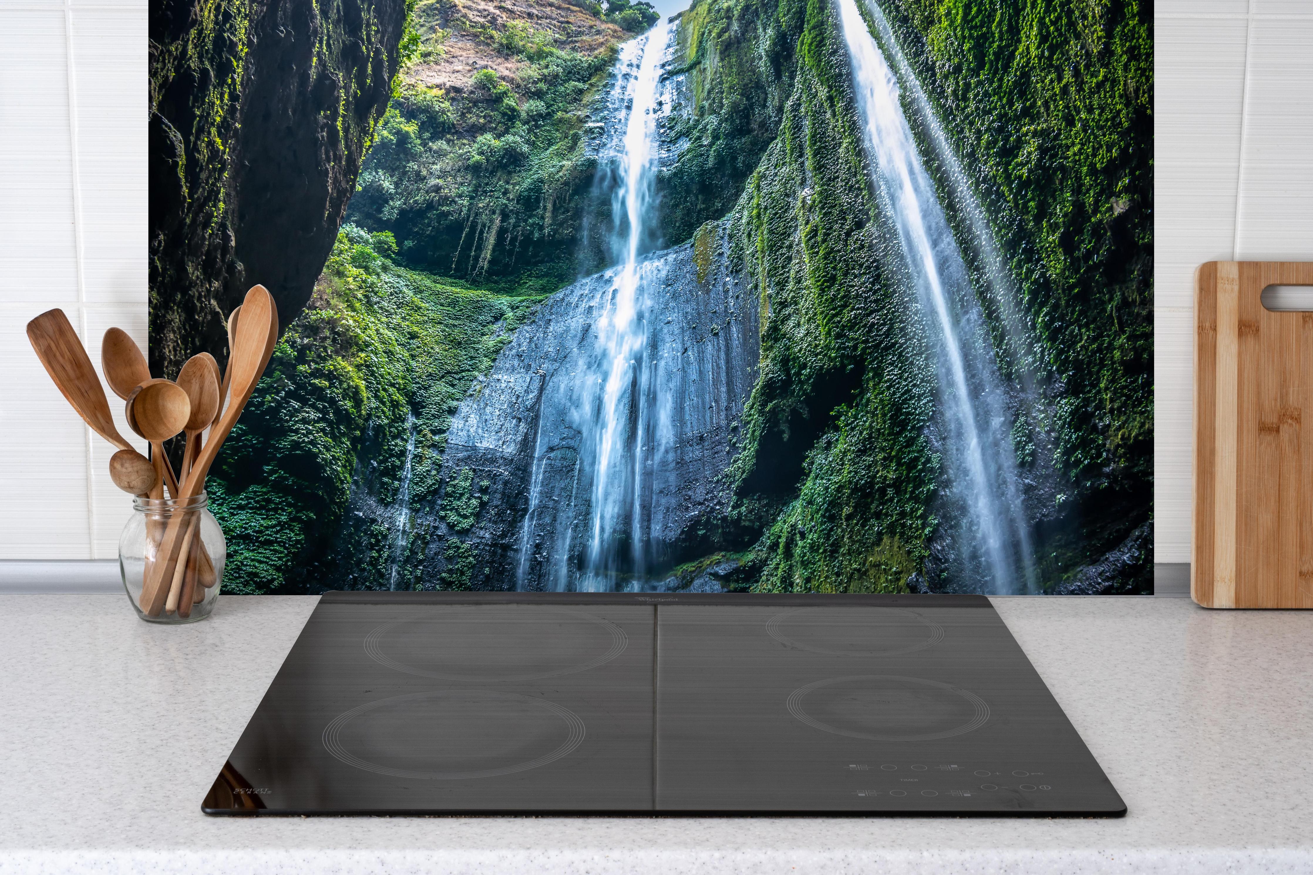 Spritzschutz - Der Madakaripura-Wasserfall in Indonesien hinter einem Cerankochfeld zwischen Holz-Kochutensilien
