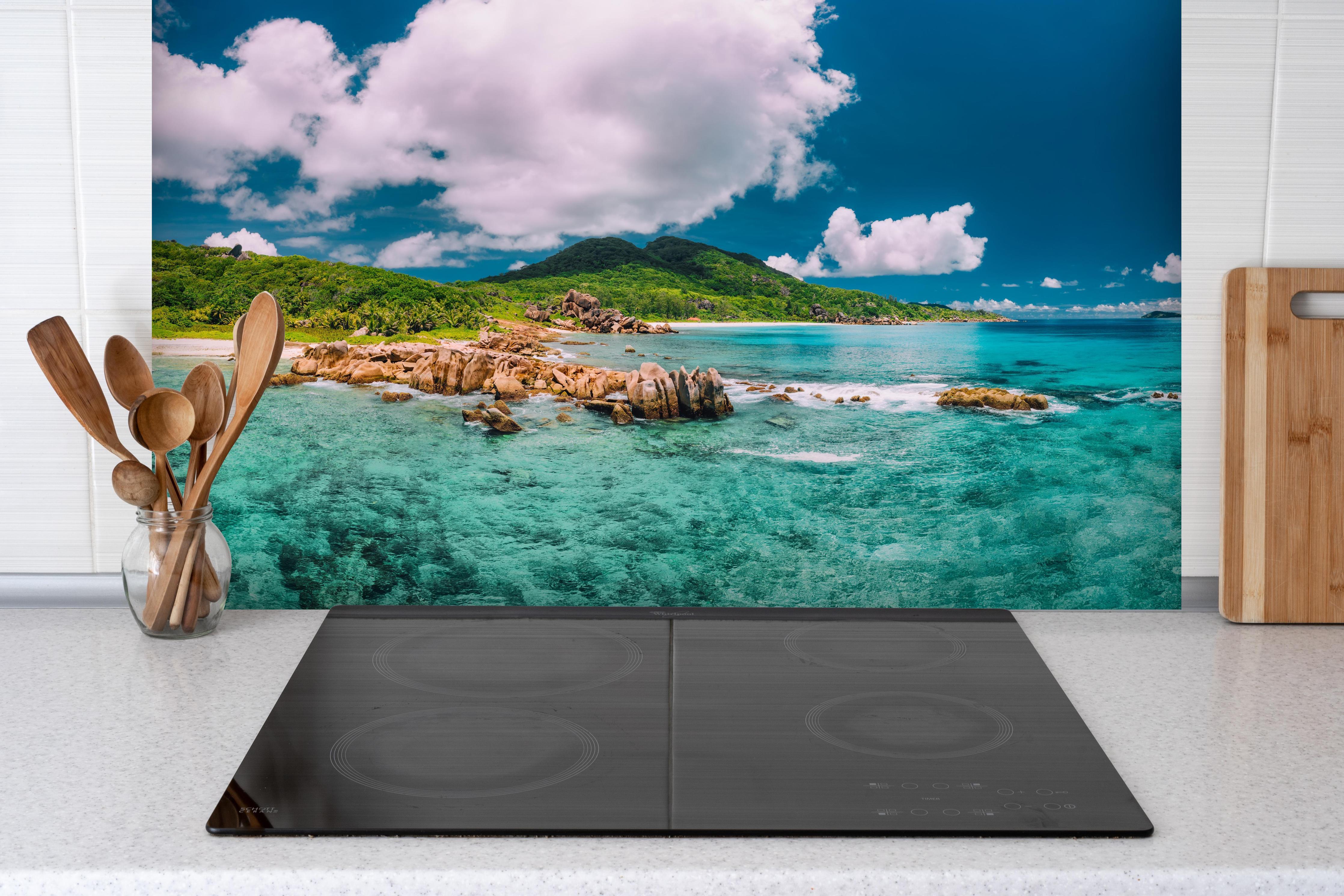 Spritzschutz - Der Strand Grand Anse - La Digue hinter einem Cerankochfeld zwischen Holz-Kochutensilien
