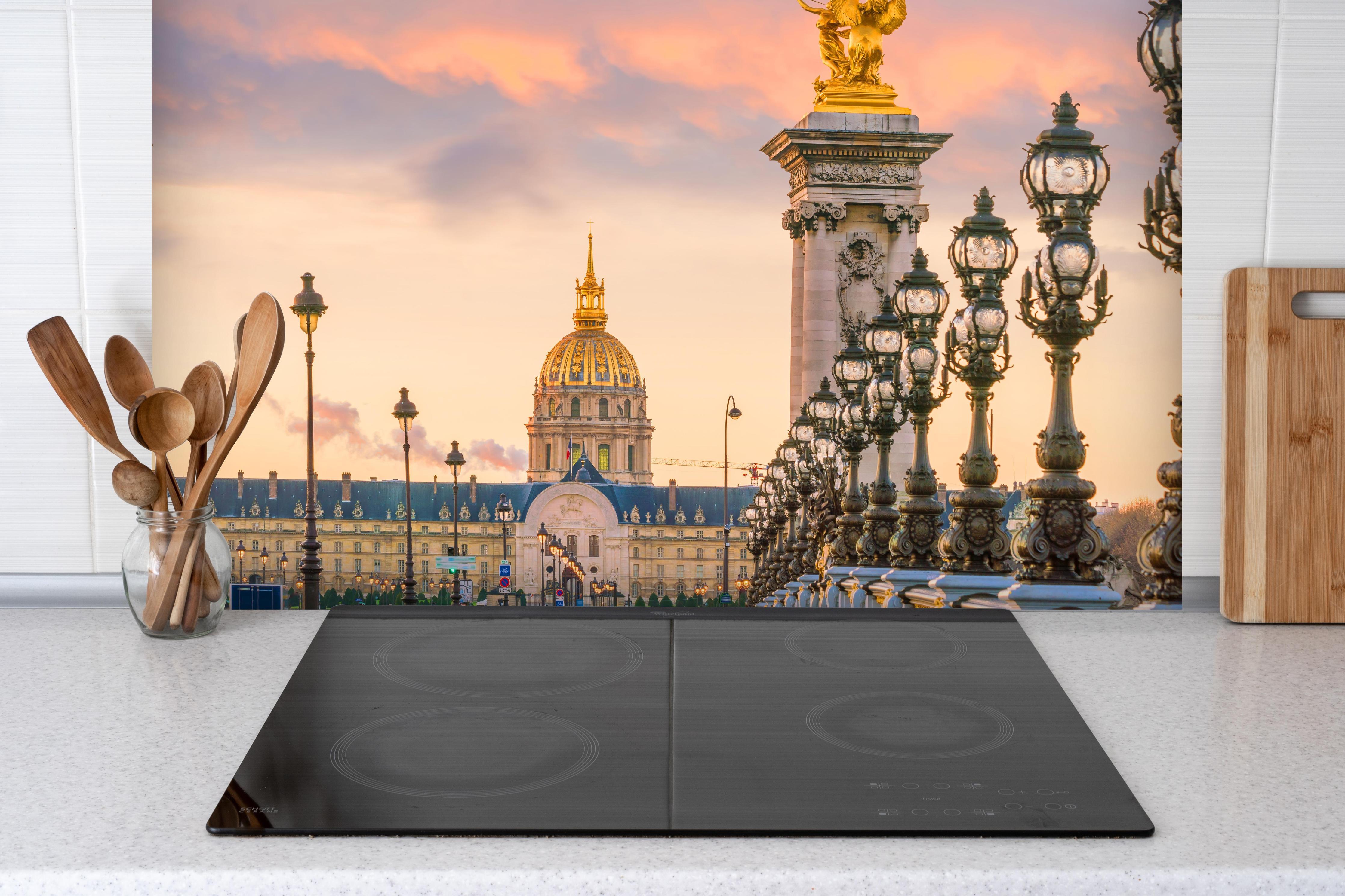 Spritzschutz - Die Pont Alexandre III Brücke über die Seine in Paris hinter einem Cerankochfeld zwischen Holz-Kochutensilien
