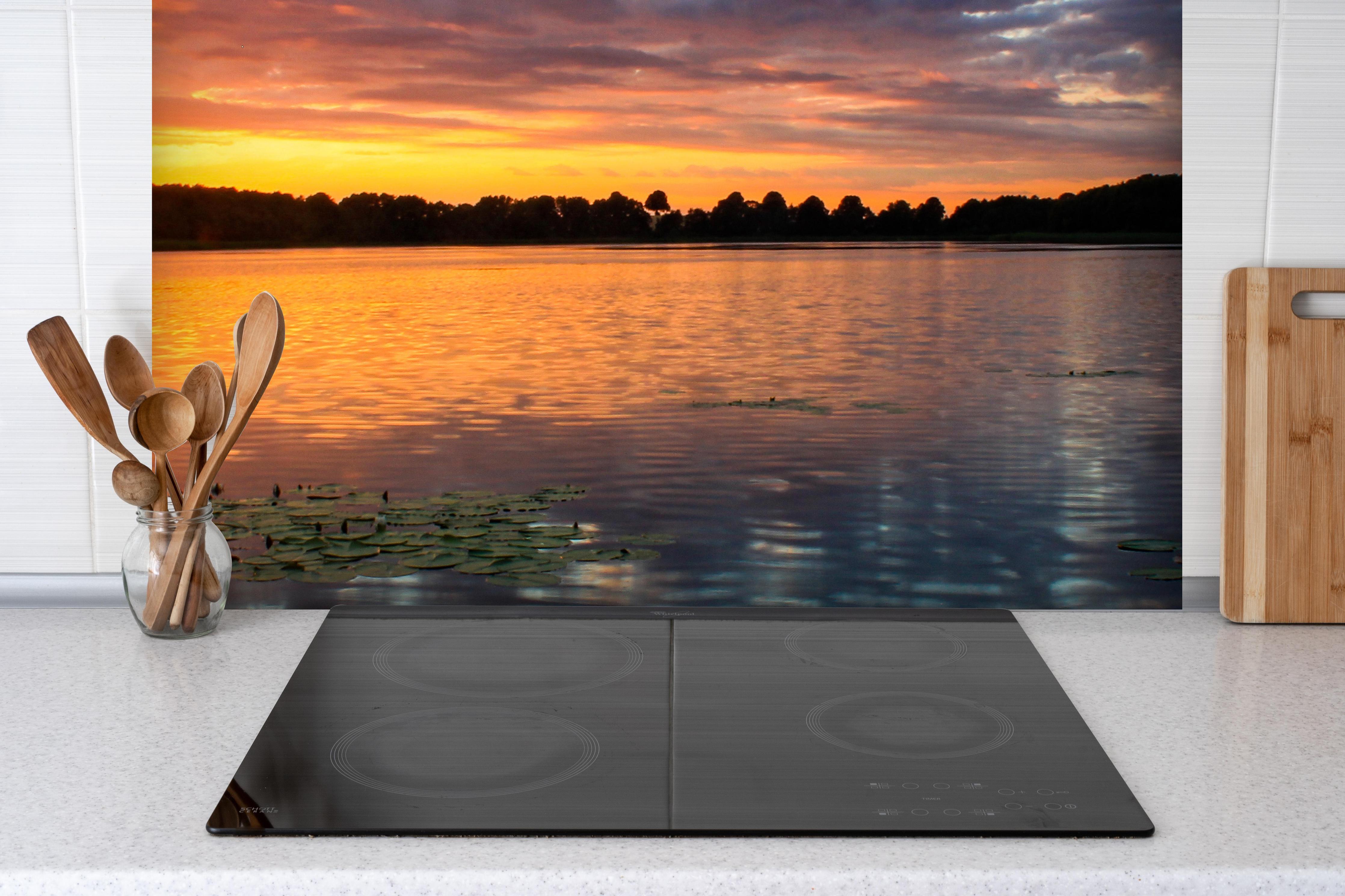 Spritzschutz - Epischer Sonnenuntergang über See hinter einem Cerankochfeld zwischen Holz-Kochutensilien
