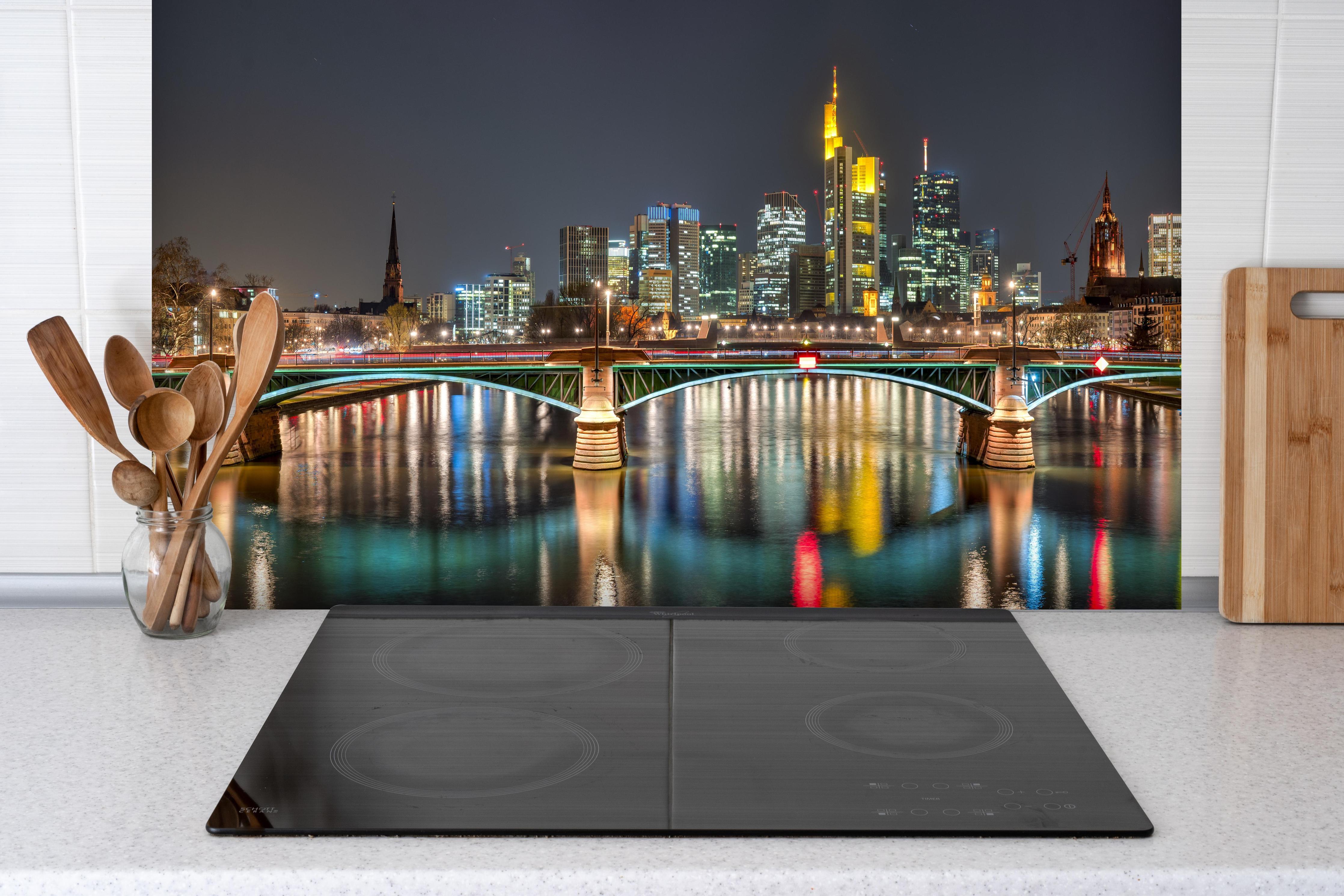 Spritzschutz - Frankfurt Skyline bei Nacht hinter einem Cerankochfeld zwischen Holz-Kochutensilien
