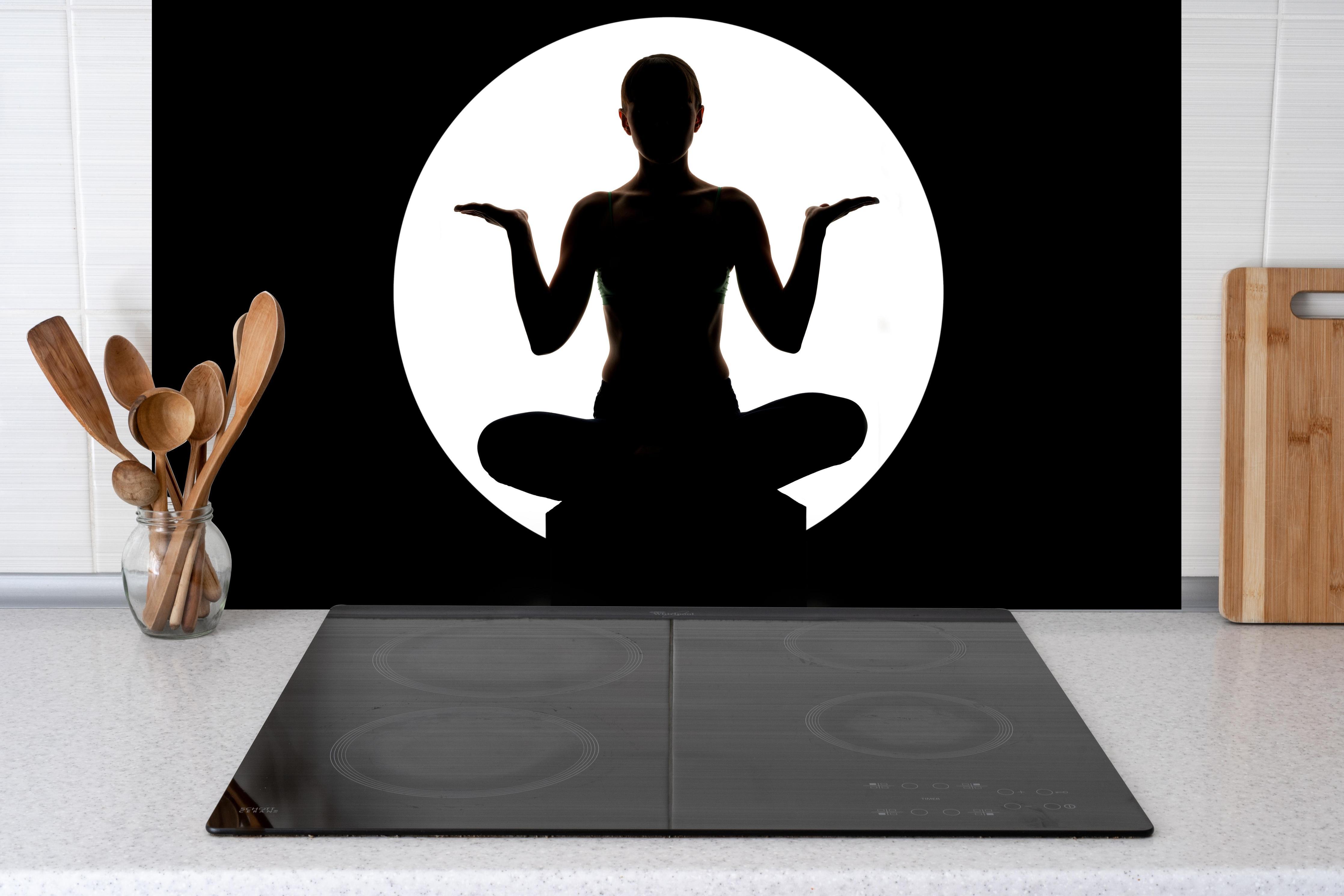 Spritzschutz - Frau Silhouette sitzt in Yoga-Pose hinter einem Cerankochfeld zwischen Holz-Kochutensilien
