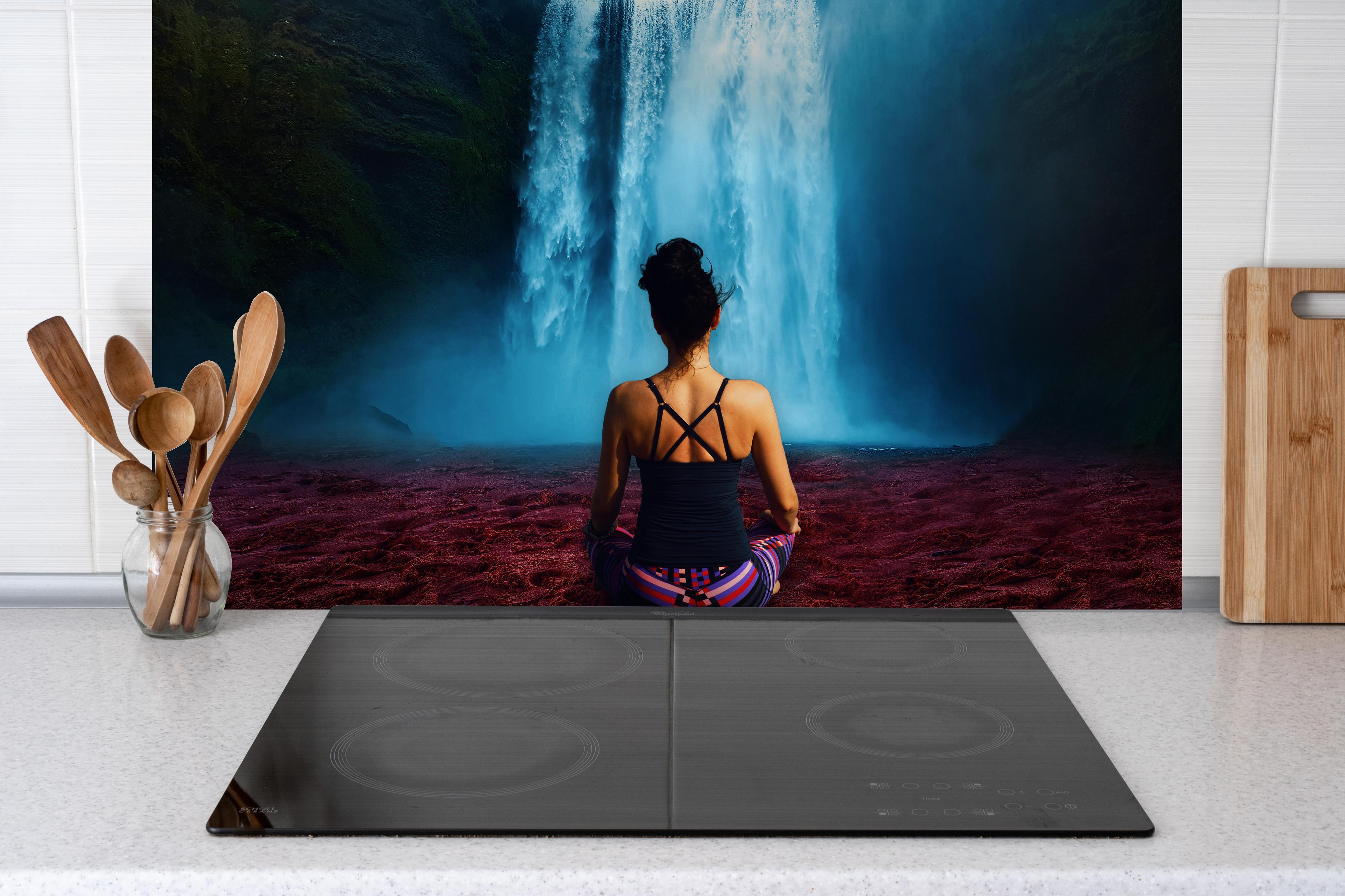 Spritzschutz - Frau meditierend vor traumhaften Wasserfall hinter einem Cerankochfeld zwischen Holz-Kochutensilien
