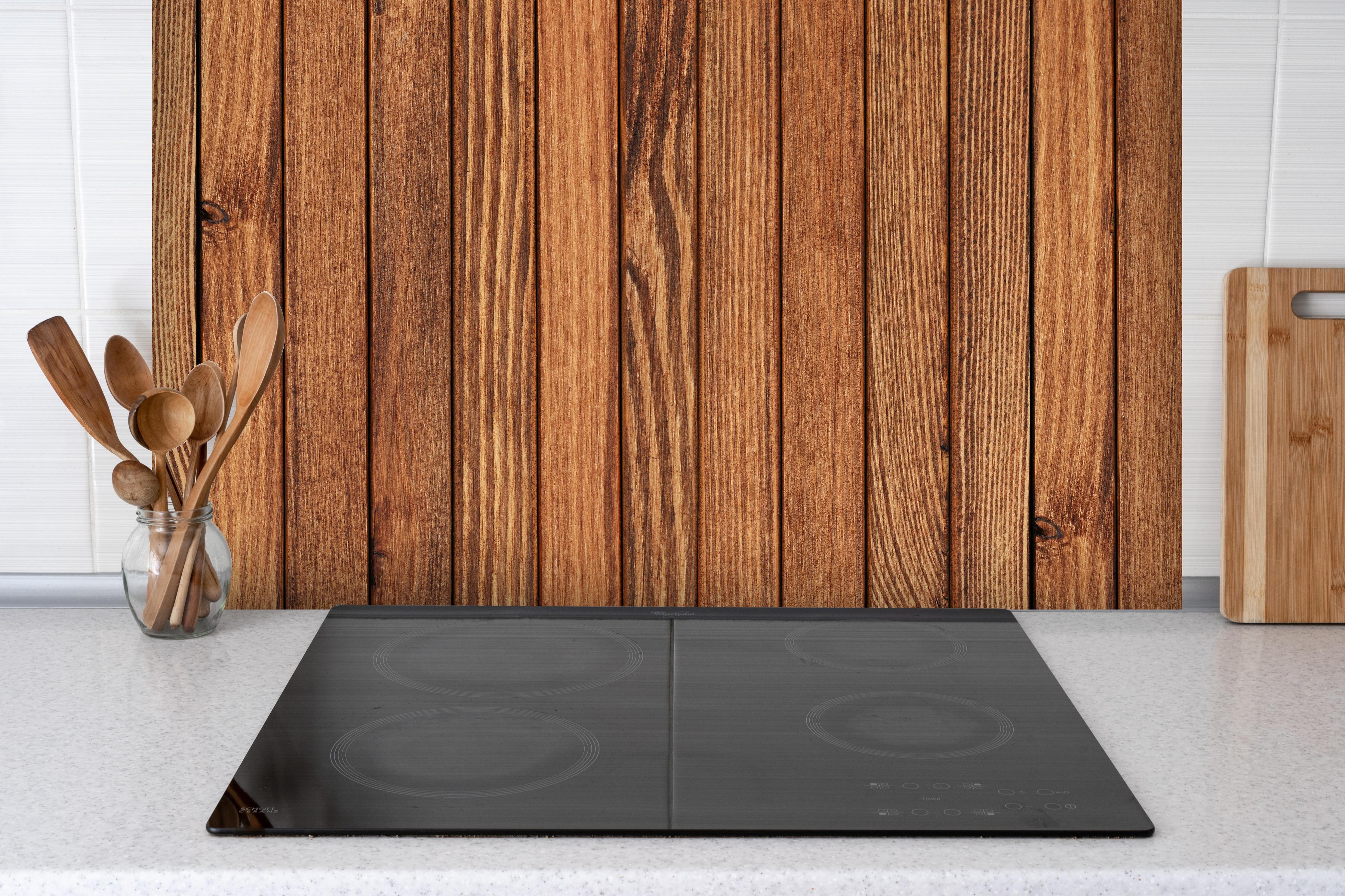 Spritzschutz - Gestreifte natürliche Holzbretter hinter einem Cerankochfeld zwischen Holz-Kochutensilien
