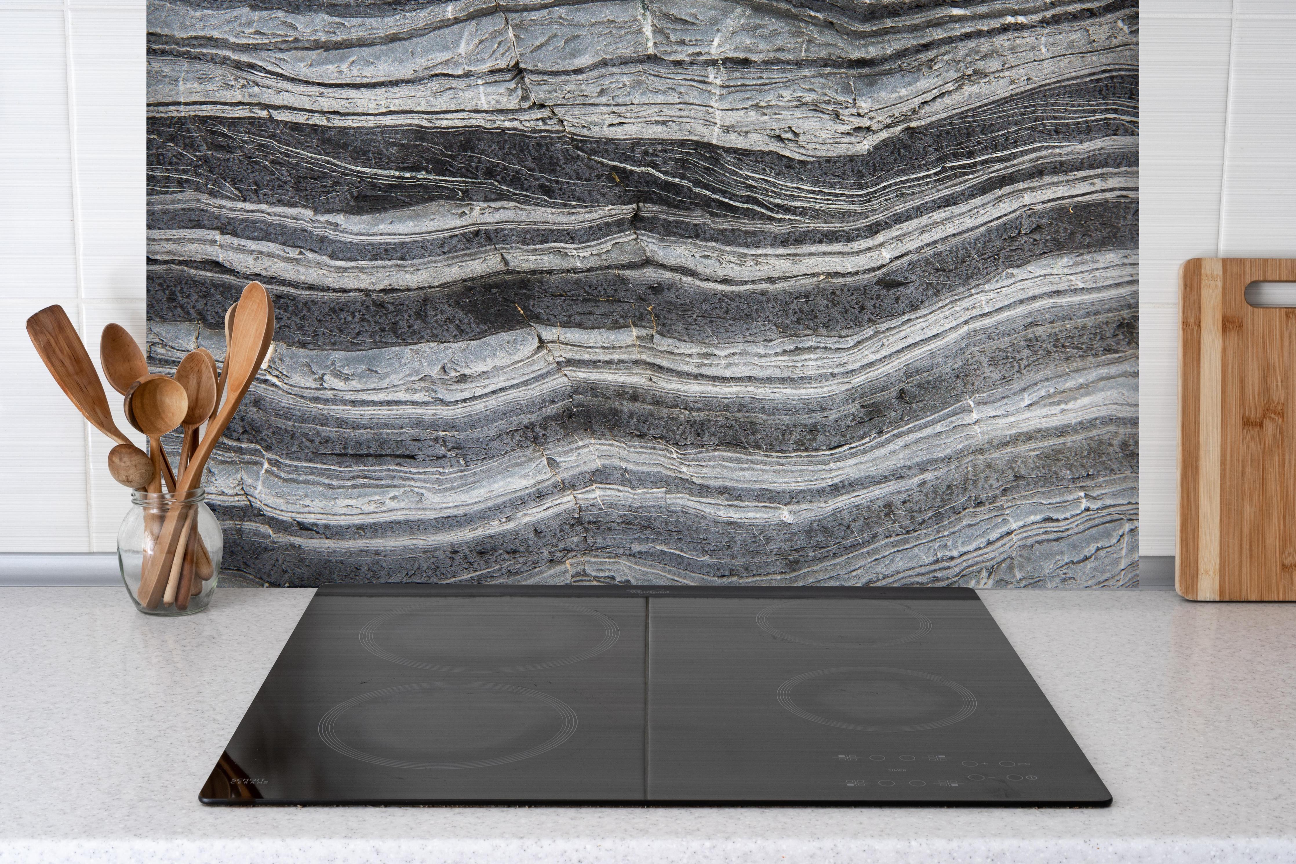 Spritzschutz - Gräulicher rissiger Schiefer hinter einem Cerankochfeld zwischen Holz-Kochutensilien
