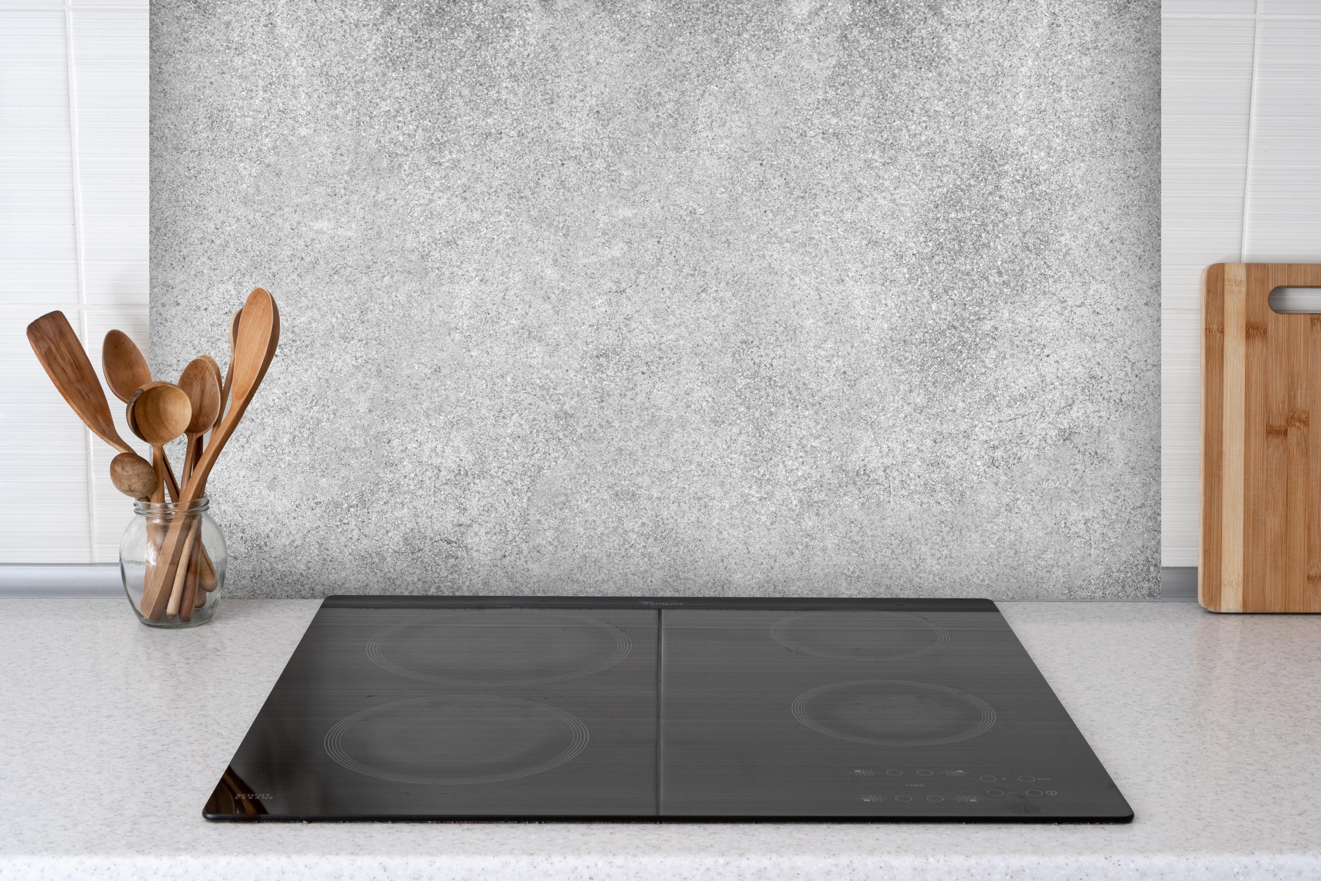 Spritzschutz - Grauer Kalkstein hinter einem Cerankochfeld zwischen Holz-Kochutensilien
