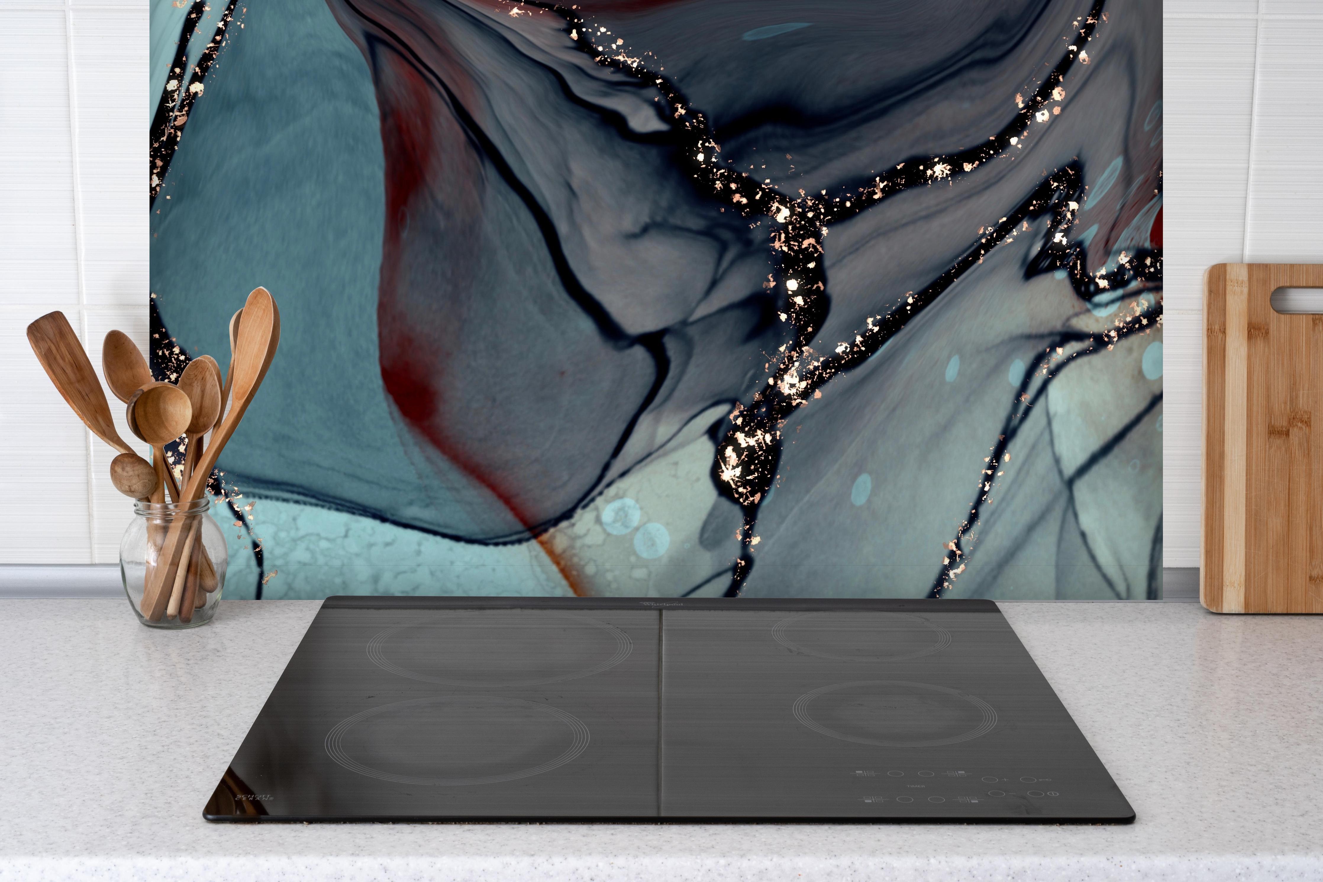 Spritzschutz - Grünliche Tinte mit Goldelementen hinter einem Cerankochfeld zwischen Holz-Kochutensilien
