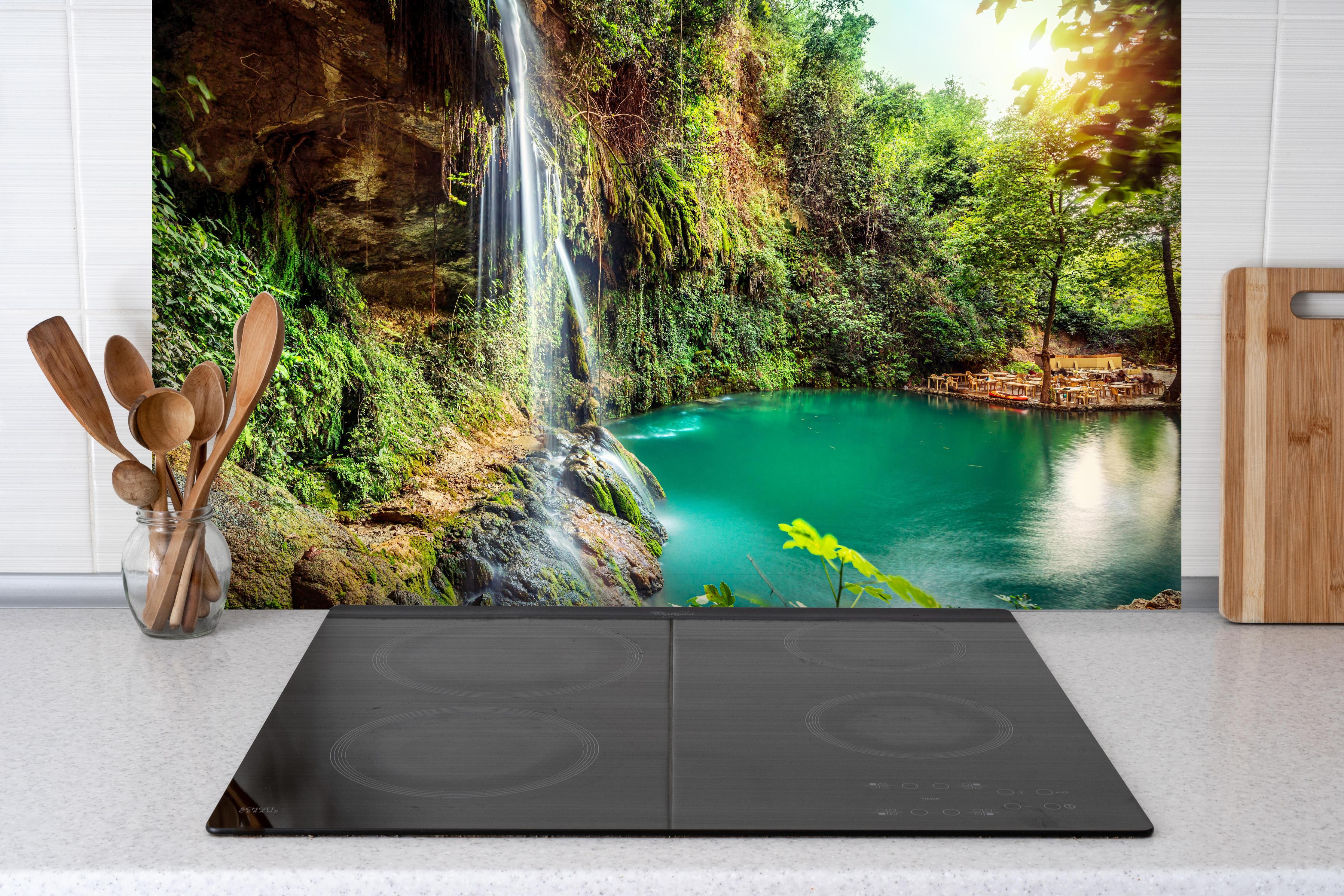 Spritzschutz - Kaskade mit klarem Bach im Libanon hinter einem Cerankochfeld zwischen Holz-Kochutensilien
