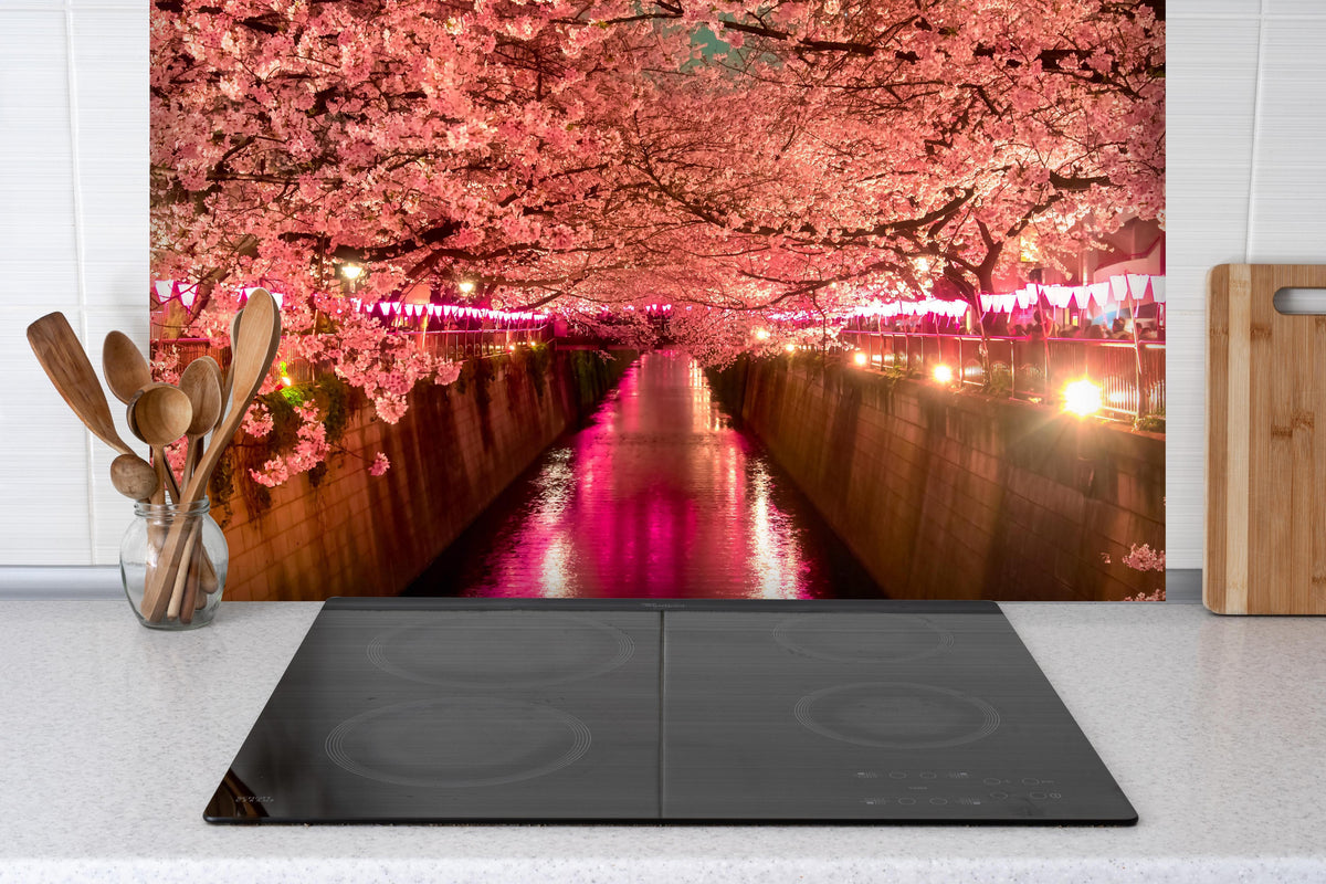 Spritzschutz - Kirschblüten bei Nacht in Tokio hinter einem Cerankochfeld zwischen Holz-Kochutensilien
