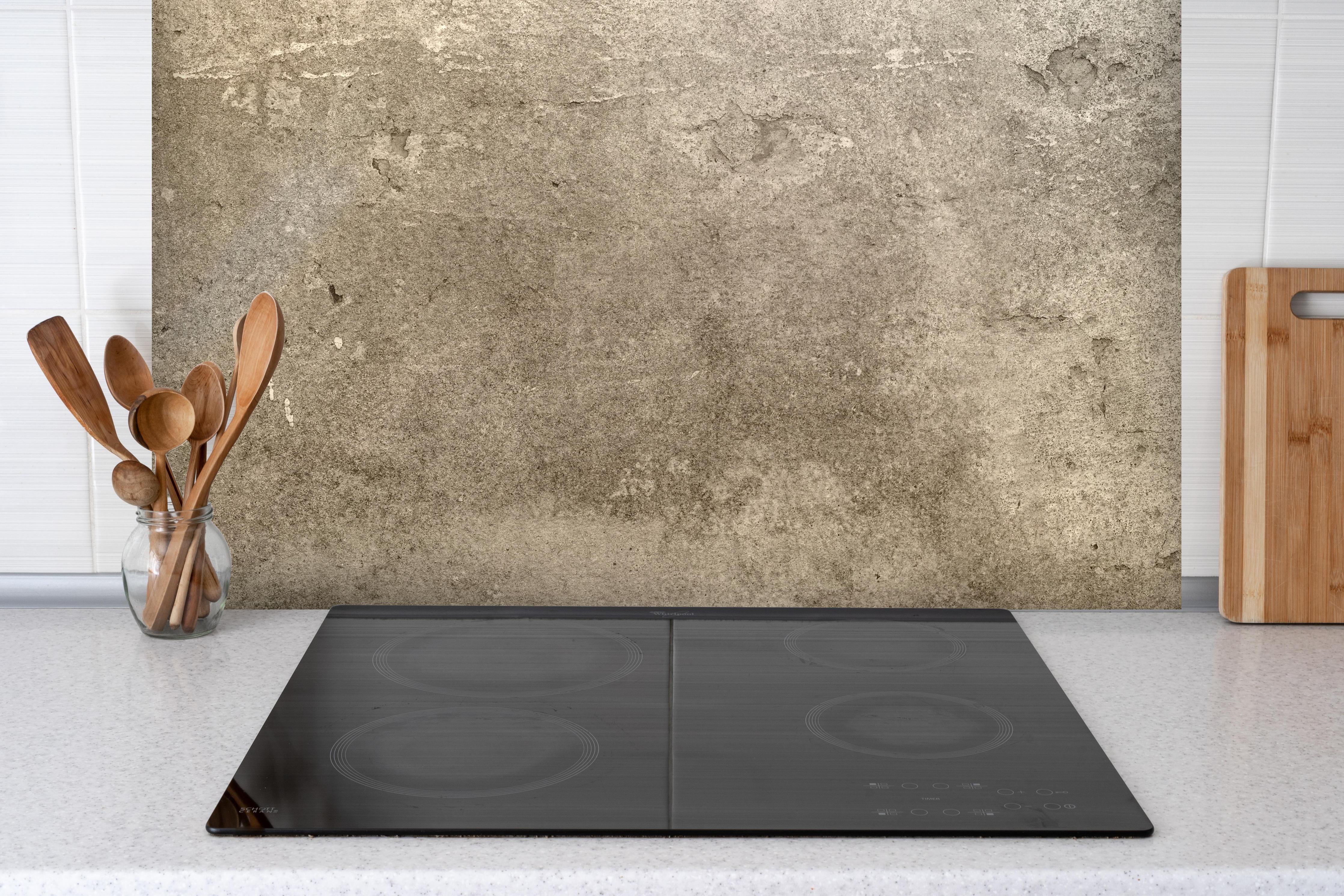 Spritzschutz - Massiver beigefarbiger Beton hinter einem Cerankochfeld zwischen Holz-Kochutensilien
