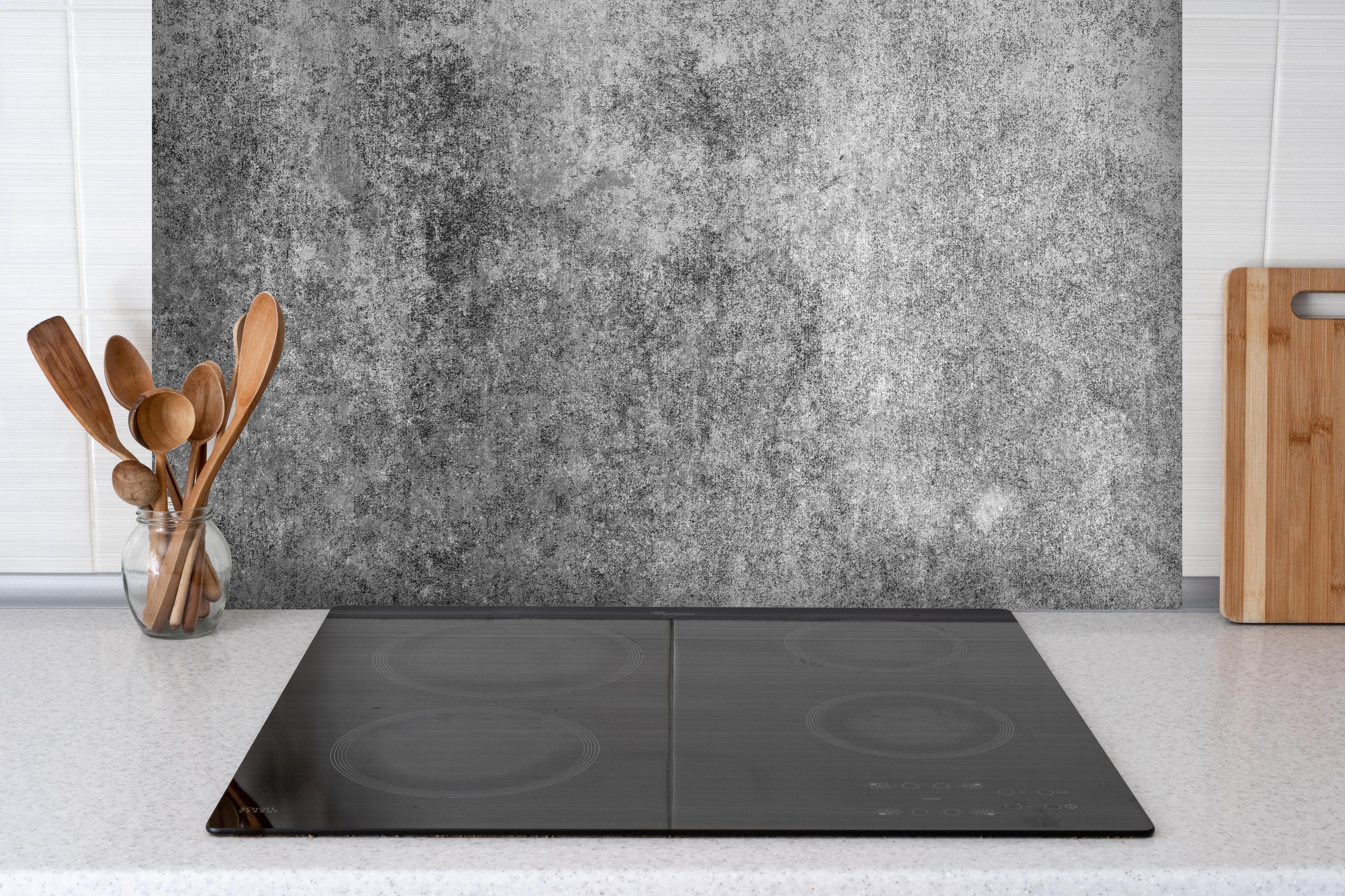 Spritzschutz - Massiver dunkelgrauer Beton hinter einem Cerankochfeld zwischen Holz-Kochutensilien
